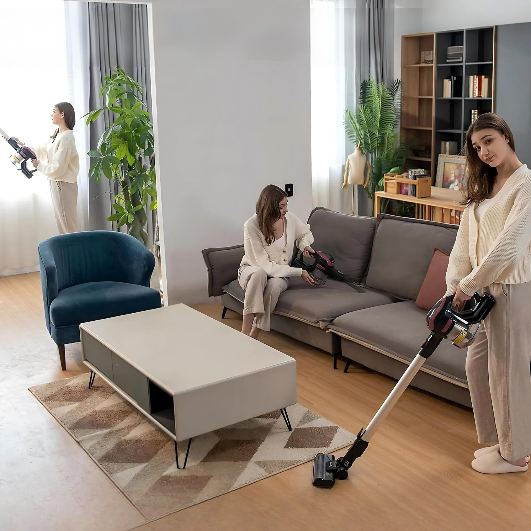 Trzy kobiety odkurzają salon. Jedna przy oknie, jedna na sofie, a jedna stojąca. Neutralna kolorystyka.