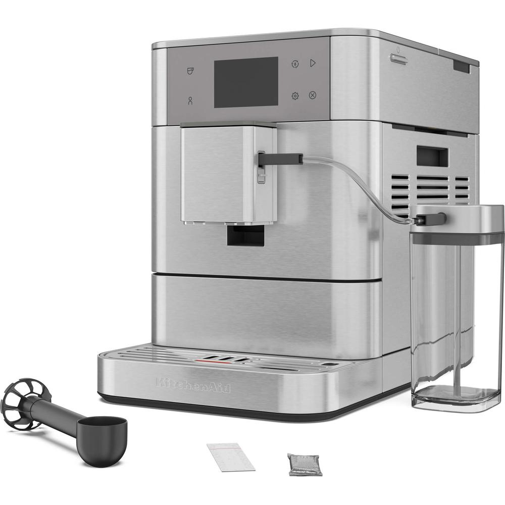 Eine silberne KitchenAid Espressomaschine mit Zubehör. Enthält einen Aufschäumer, einen Löffel und zwei kleine Päckchen, alles auf weißem Hintergrund.
