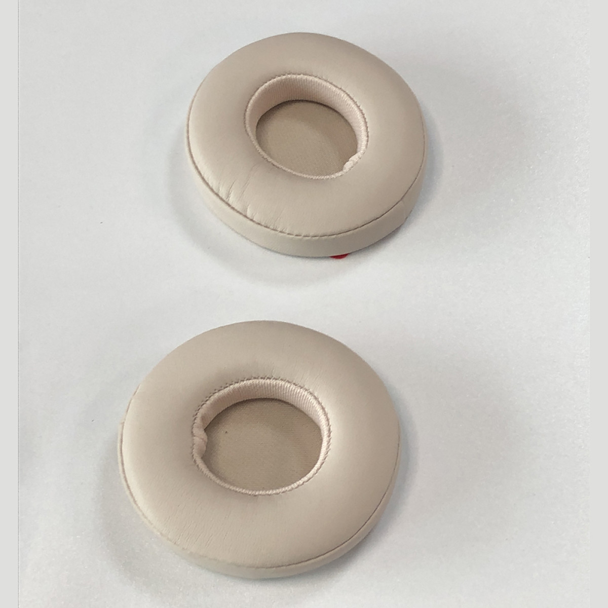 Twee beige oorkussens voor hoofdtelefoons op een wit oppervlak. Elk kussen is cirkelvormig met een centraal gat.