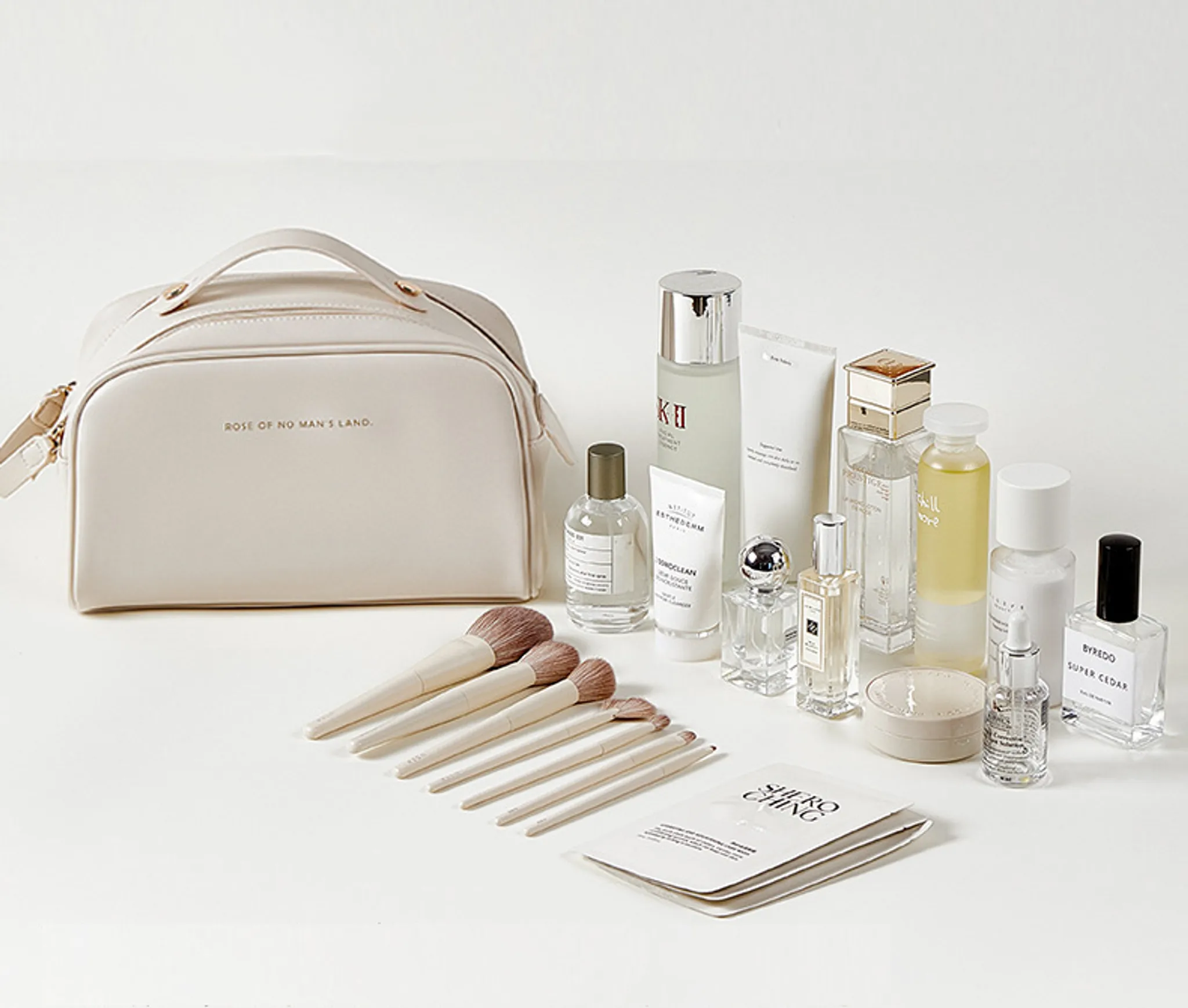 Eine beige Kosmetiktasche mit Pinseln und verschiedenen Hautpflegeflaschen auf weißer Fläche.