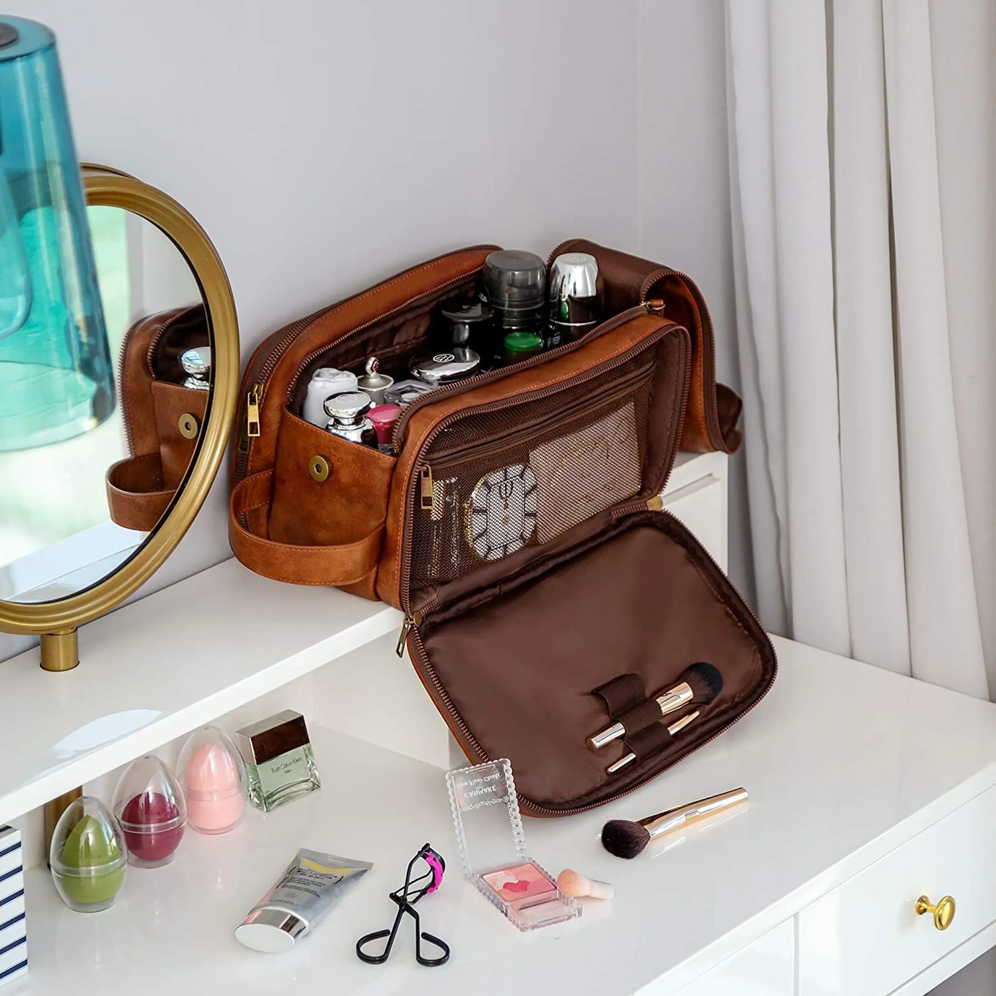 Braune Kulturtasche mit Make-up, Spiegel und Kosmetik auf einem weißen Schminktisch.