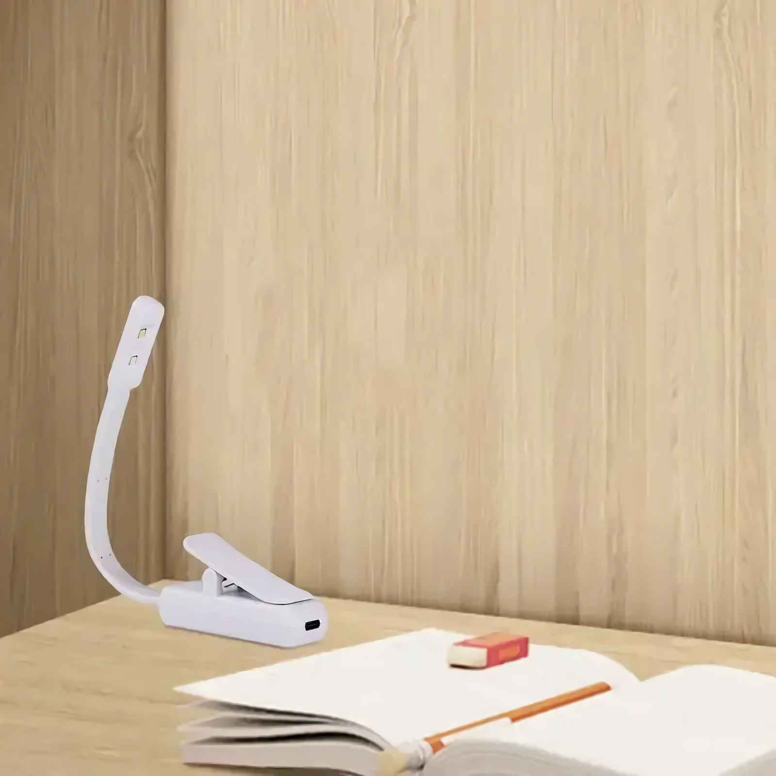 Eine weiße Klemm-LED-Buchlampe ist am Schreibtisch befestigt, mit einem offenen Buch und Bleistift.