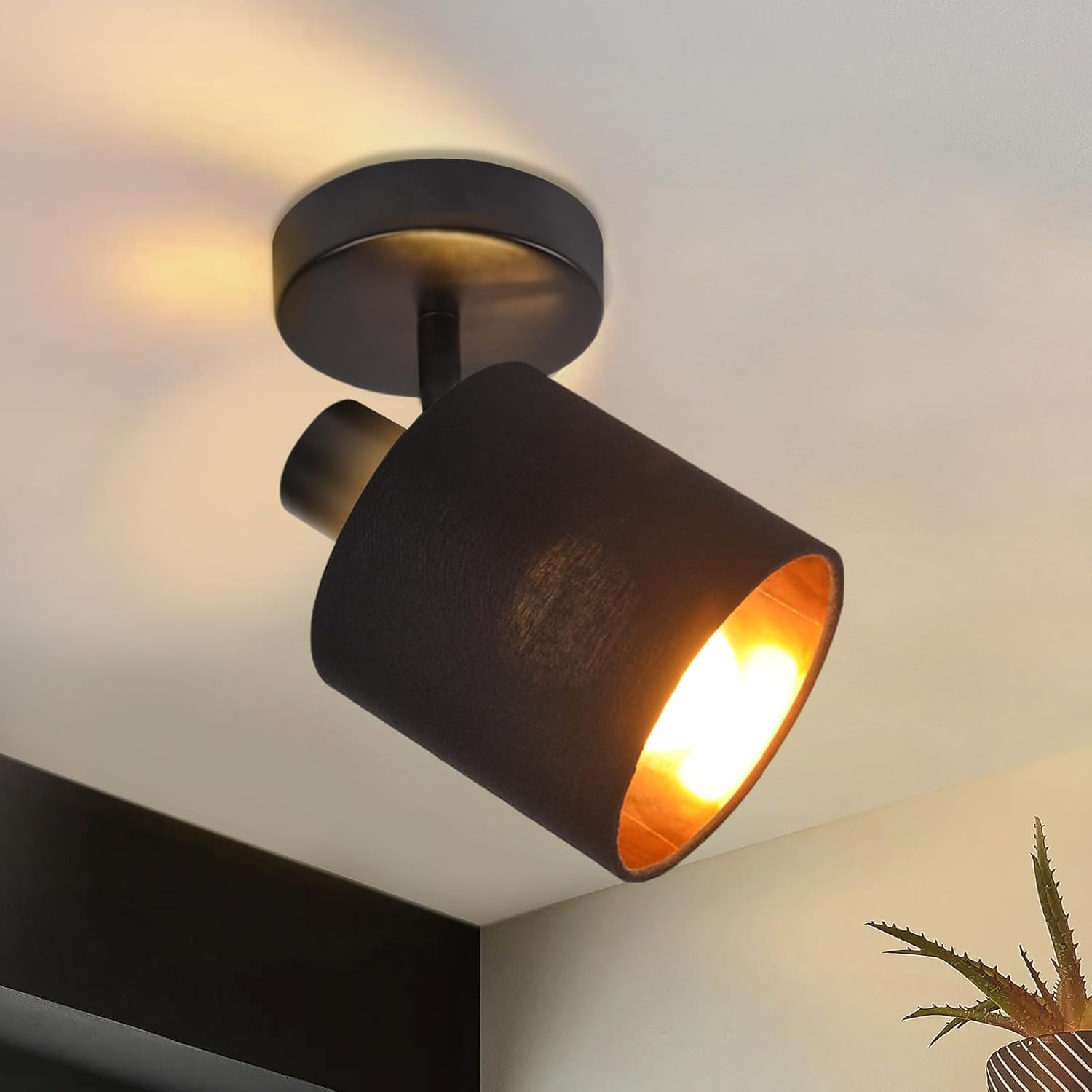 Un faretto nero con interno dorato brilla calorosamente su un soffitto bianco.