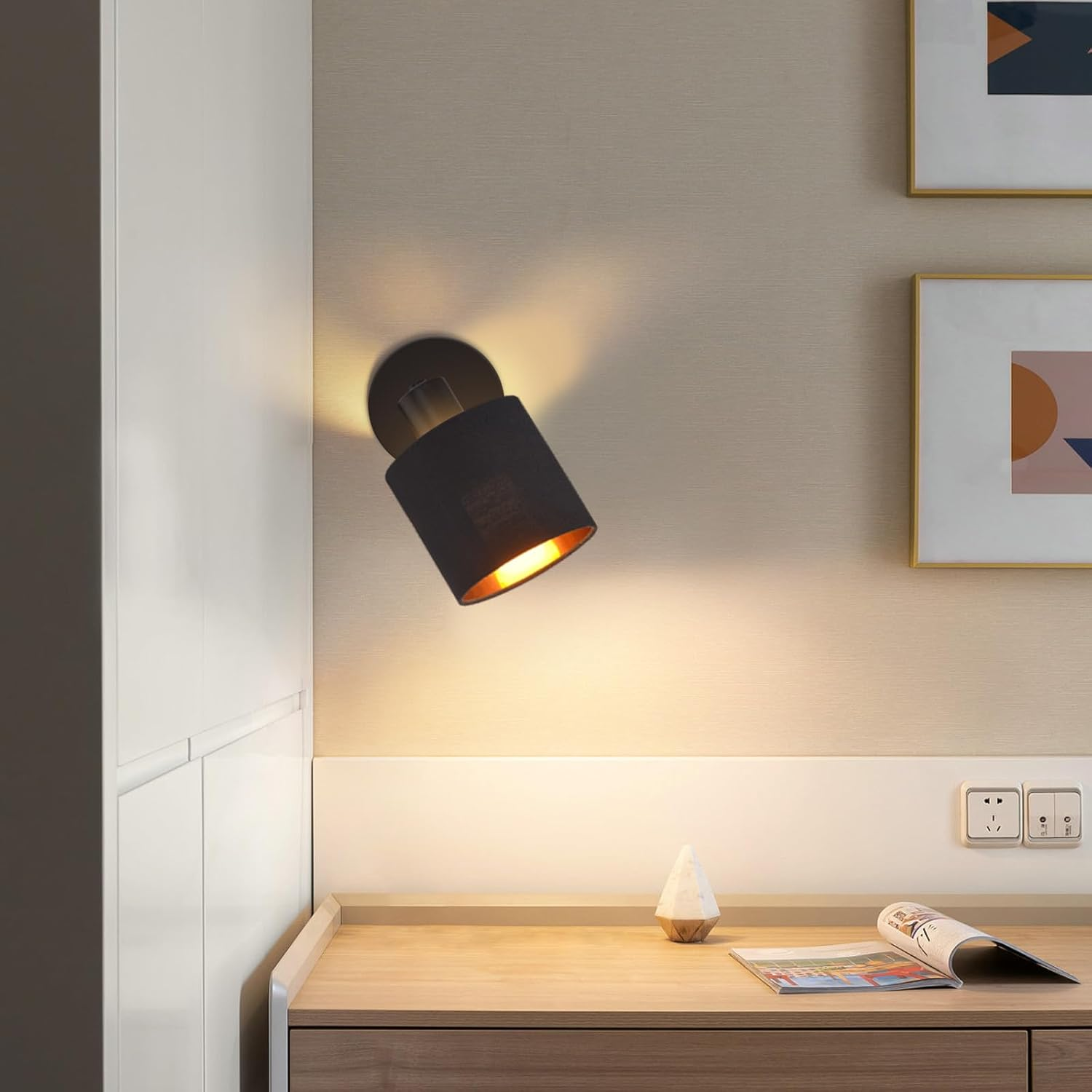 Una lampada da parete nera illumina una scrivania con rivista e oggetto decorativo.