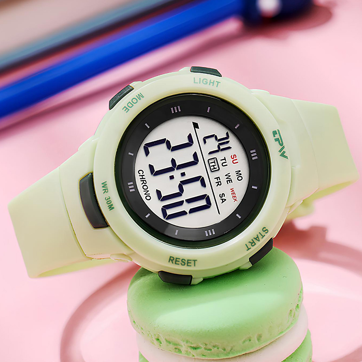 Un orologio digitale verde chiaro con pulsanti neri poggia su un macaron verde.