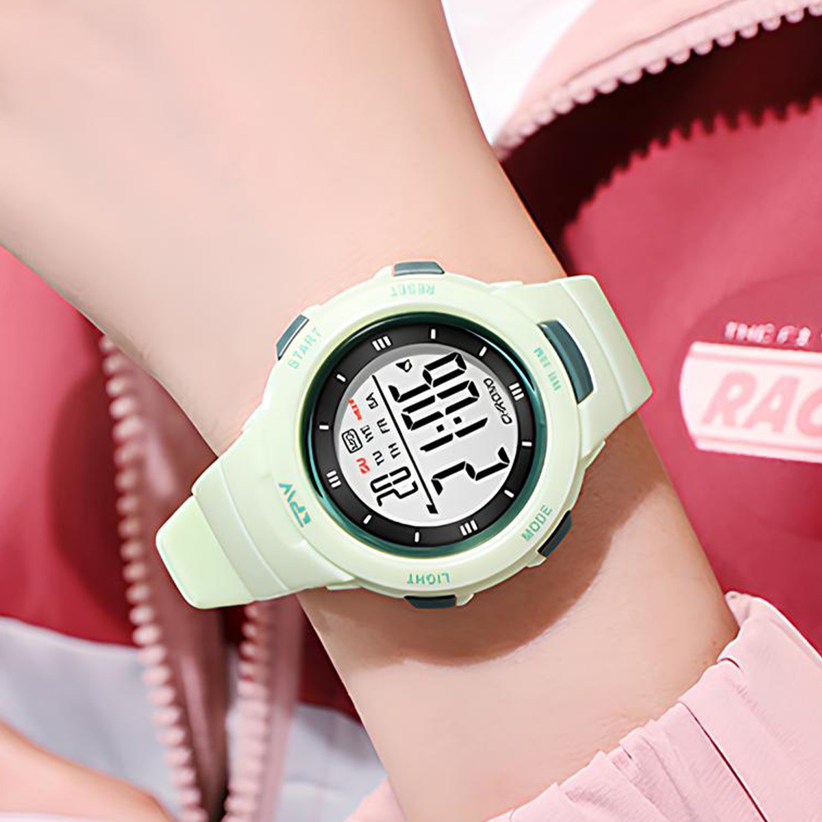 Un orologio digitale verde chiaro al polso mostra le 10:00. Sfondo di giacca rosa.
