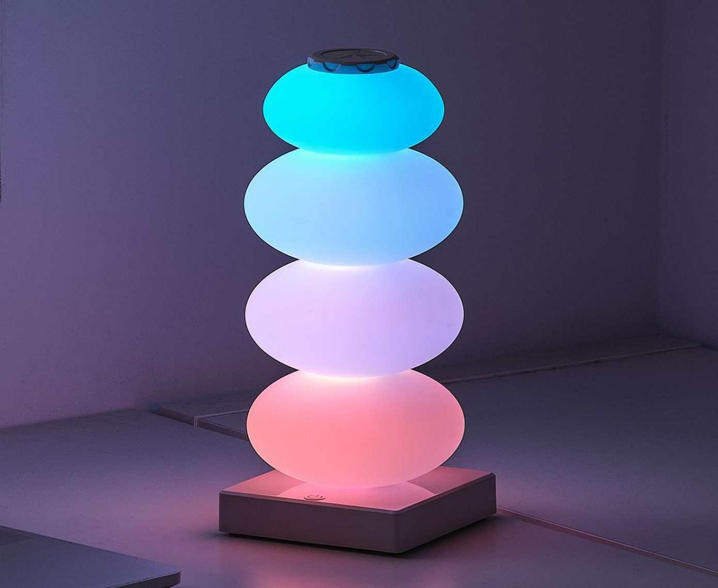Eine gestapelte Kugel-Lampe leuchtet blau, weiß, pink und rot auf einem weißen Sockel.