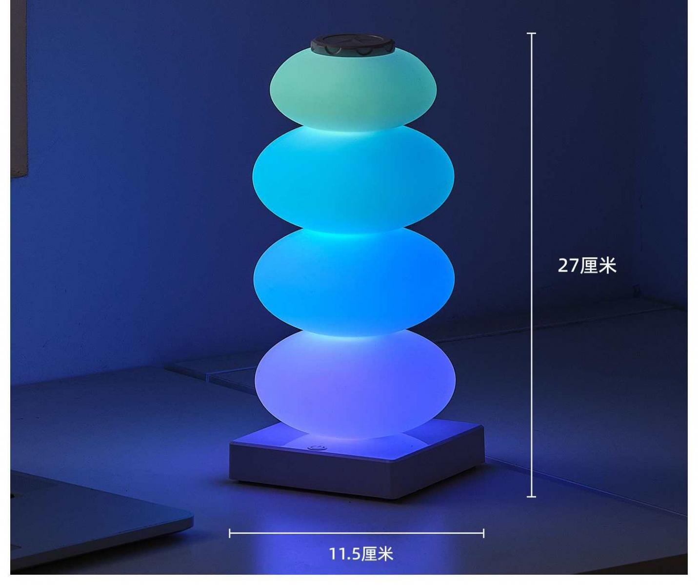 Eine gestapelte Steinlampe leuchtet blau, grün und lila auf einem Schreibtisch.