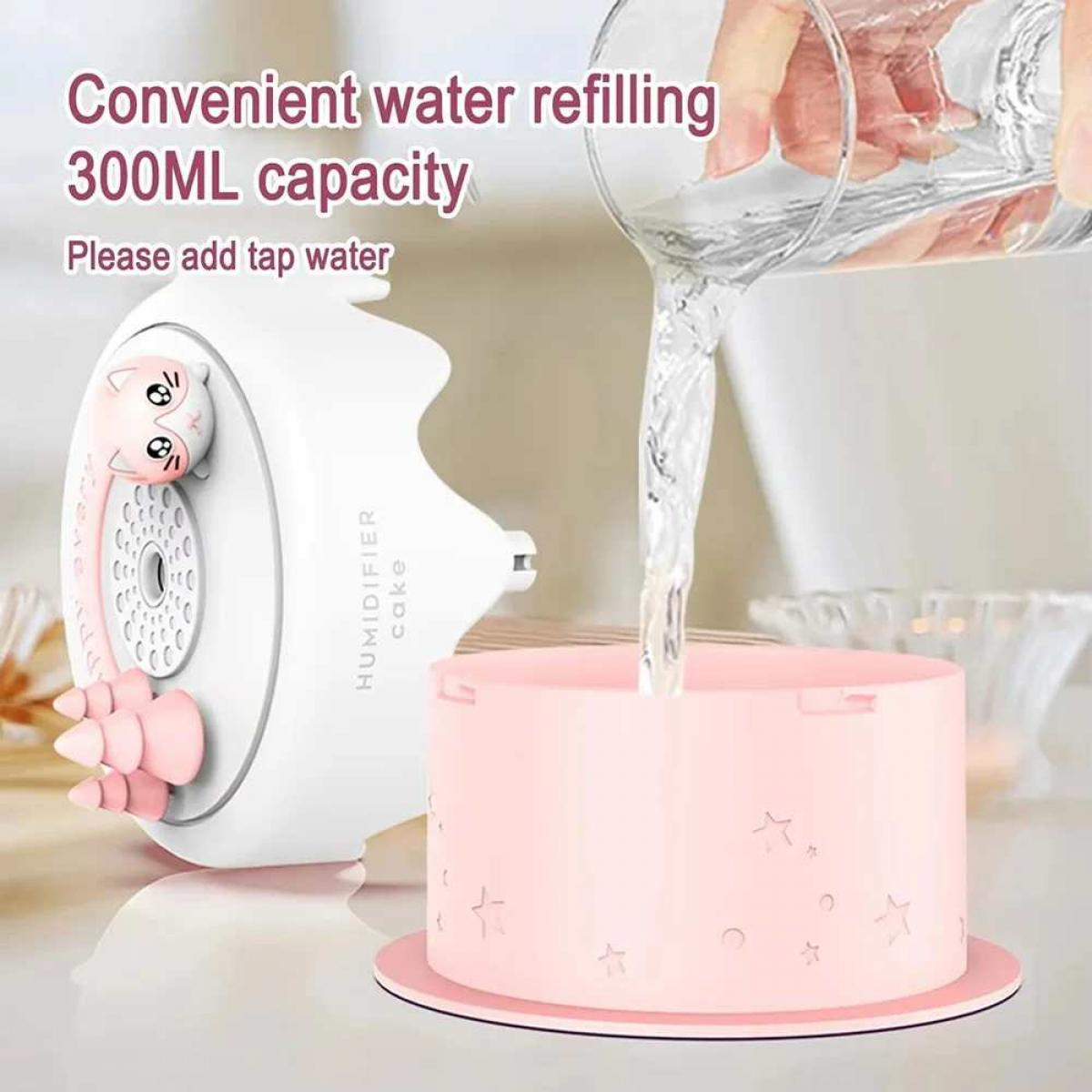Ein weißer katzenförmiger Luftbefeuchter neben einem rosa ku-chenförmigen Behälter. Wasser wird eingefüllt.