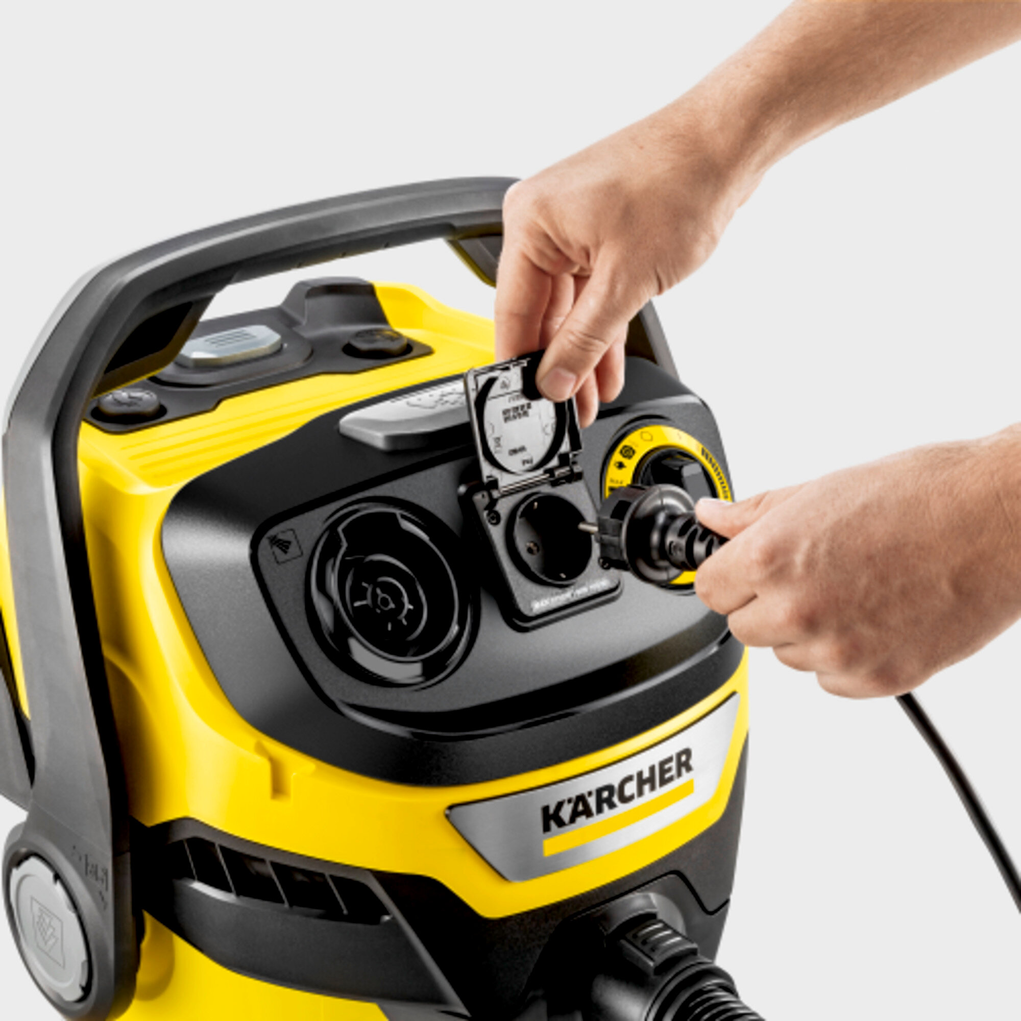 Mani inseriscono un cavo di alimentazione nero in un aspirapolvere Karcher giallo e nero.