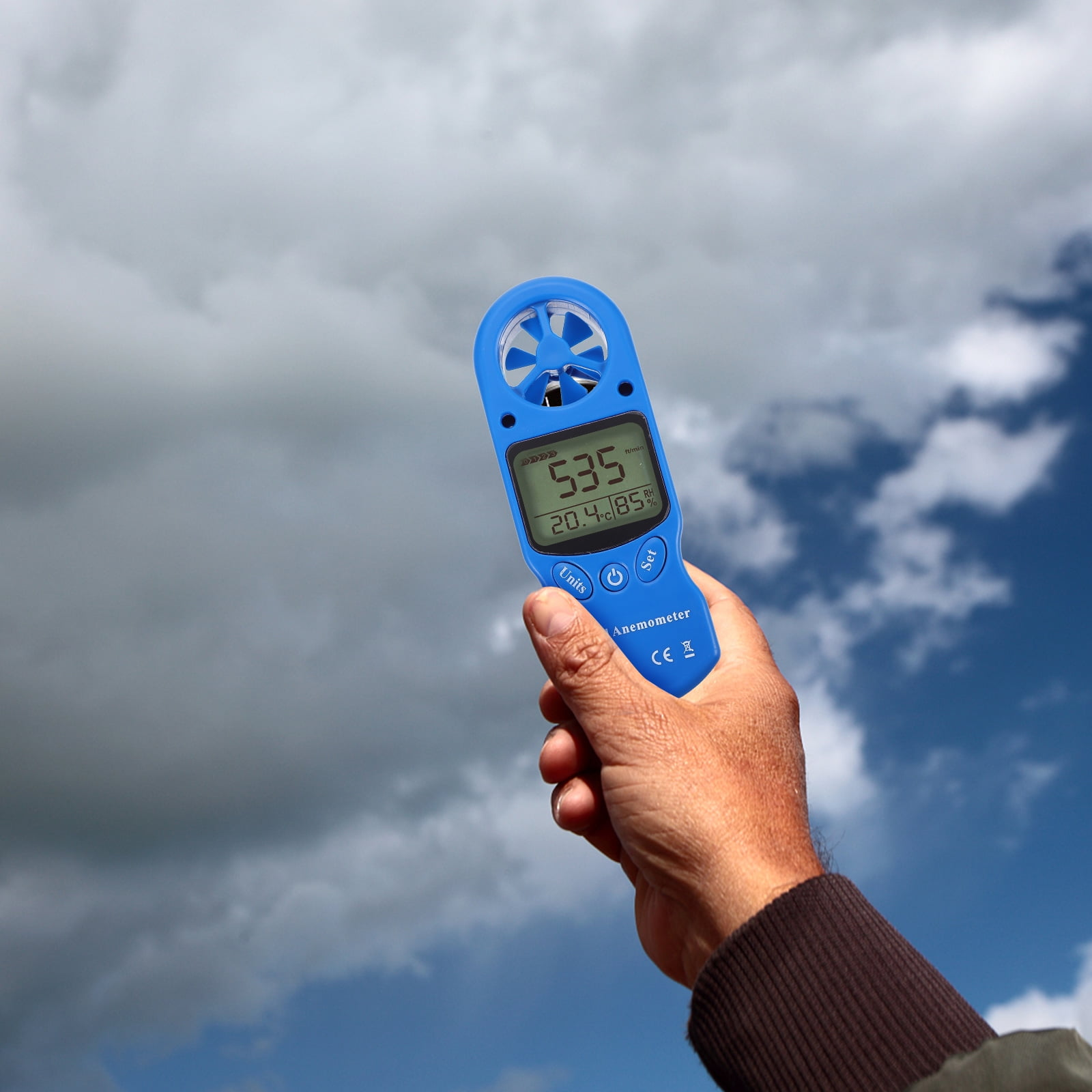 Ein blaues Anemometer vor einem bewölkten Himmel. Das Gerät zeigt 535 ft/min, 20,4°C und 85 % RH.