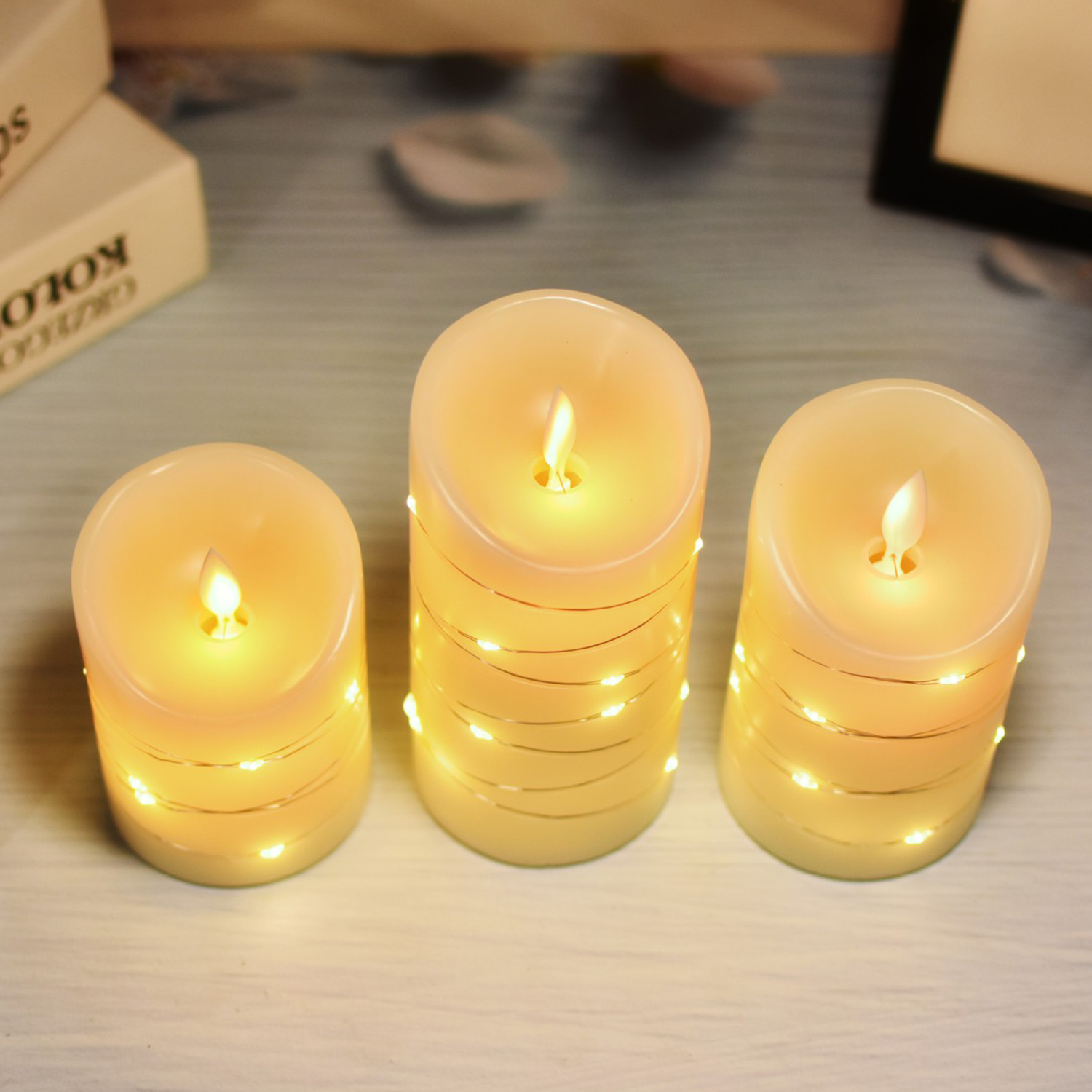 Trzy świece LED owinięte światełkami wróżki ciepło świecą na drewnianej powierzchni.