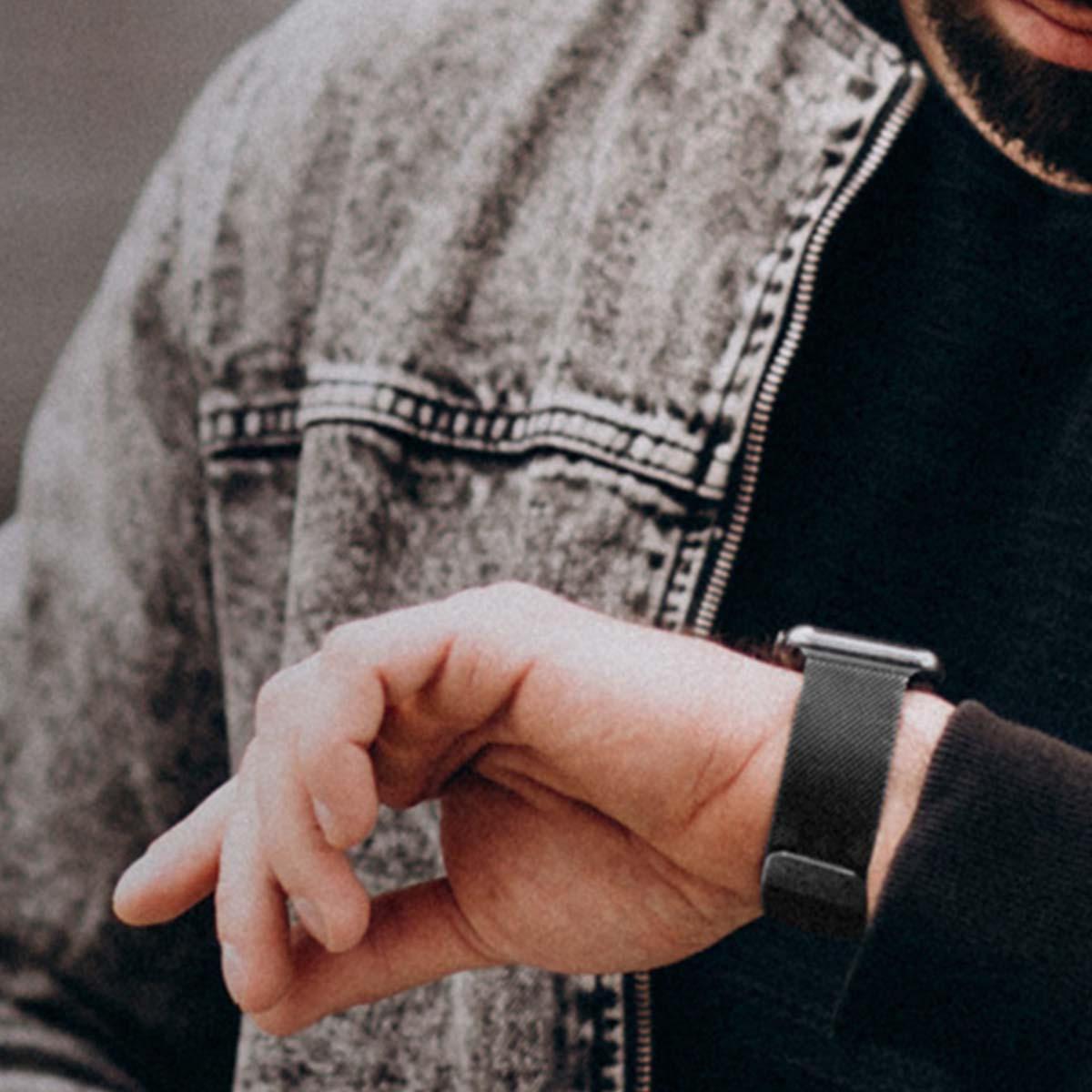 Un uomo con giacca di jeans e maglietta nera controlla l'orologio.