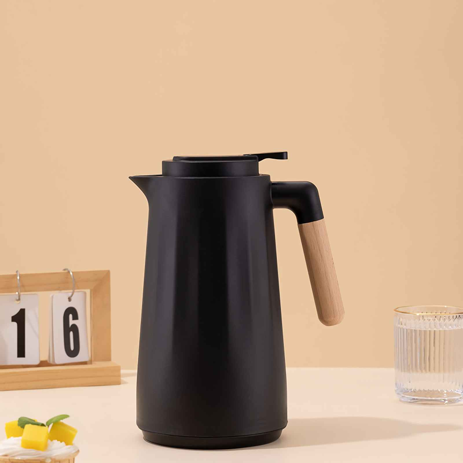 Schwarze Thermoskanne mit Holzgriff, daneben ein Glas Wasser und ein Kalender.
