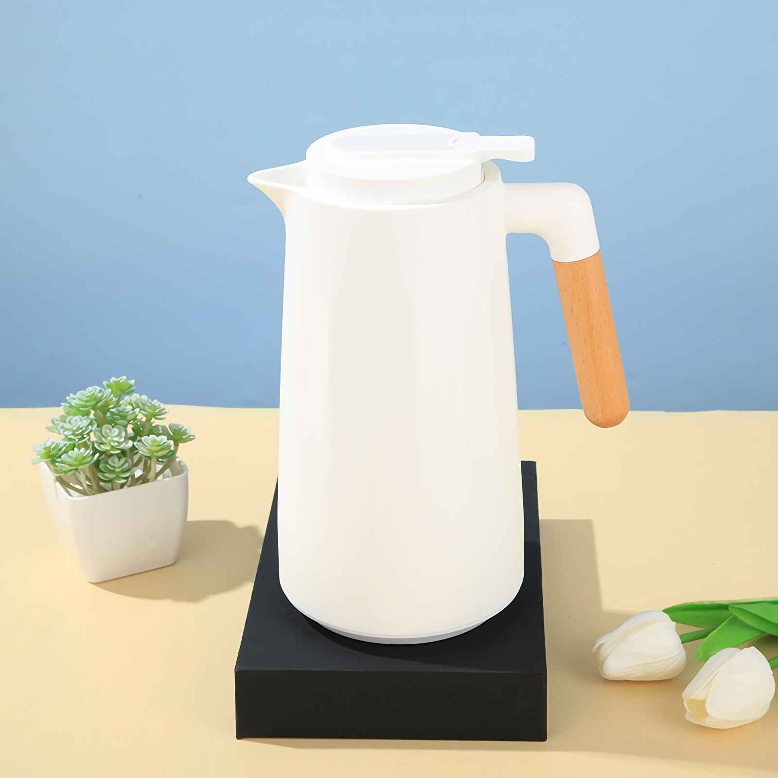 Ein weißer Thermos-Wasserkocher mit Holzgriff steht auf einem schwarzen Podest.