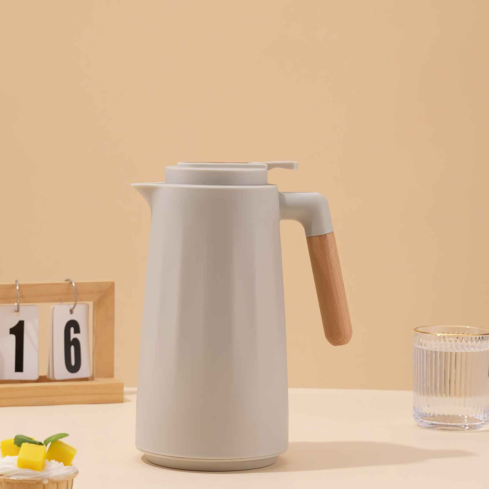 Eine weiße Thermoskanne mit Holzgriff, daneben ein Glas Wasser und ein Kalender.
