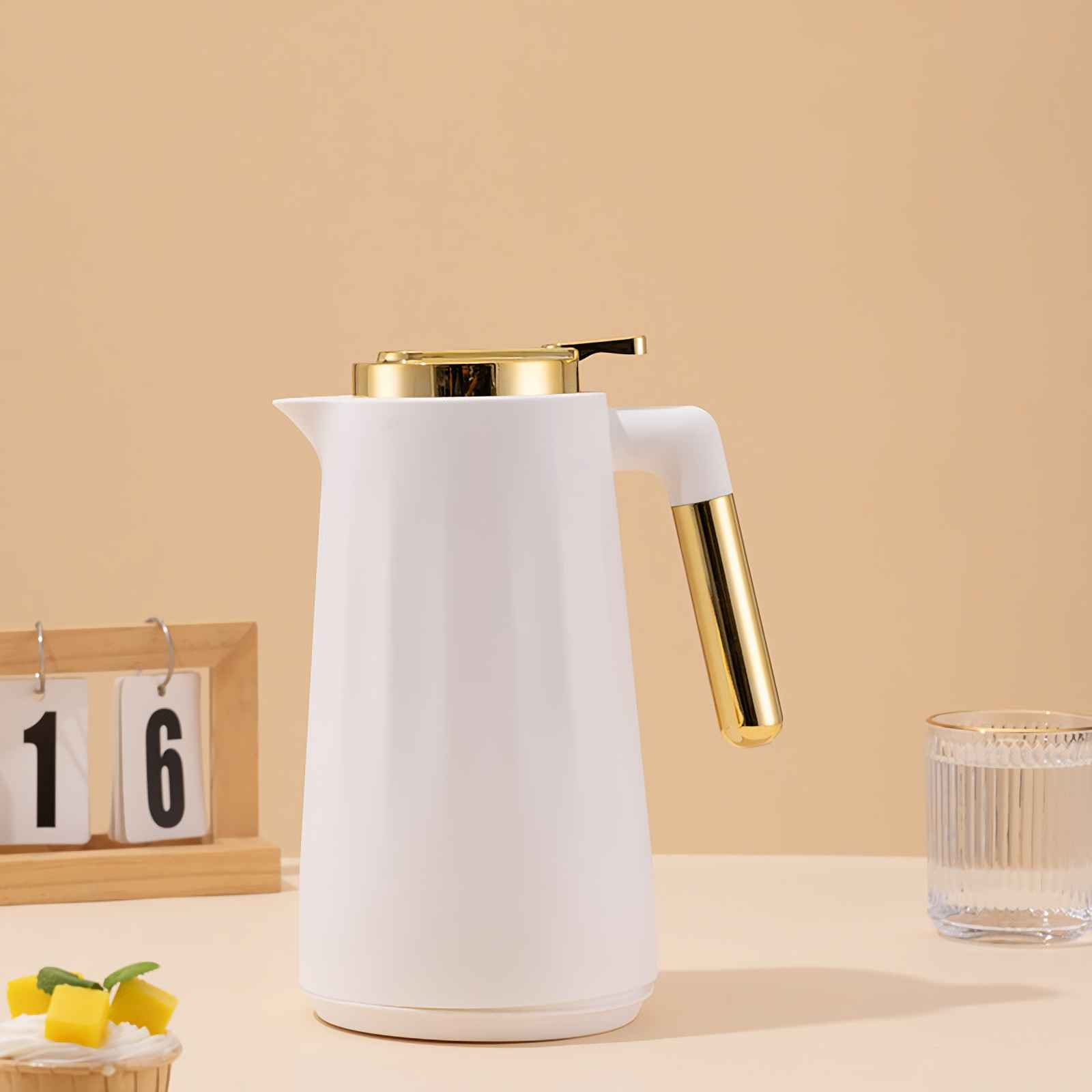 Ein weißer Thermosbehälter mit goldenen Akzenten steht neben einem Glas Wasser.
