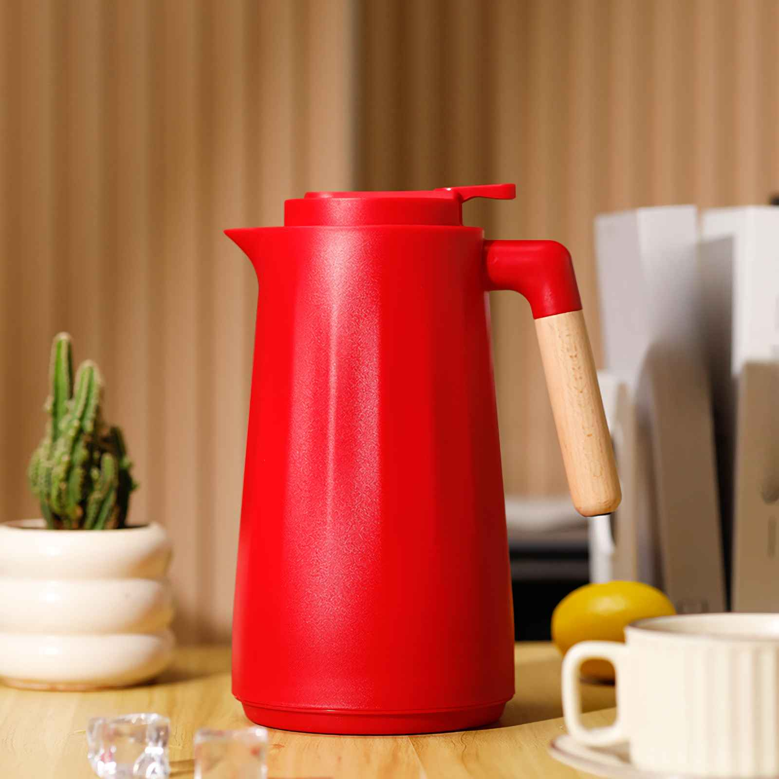 Eine rote Thermoskanne mit Holzgriff steht auf einem Tisch neben einer Kaktuspflanze.