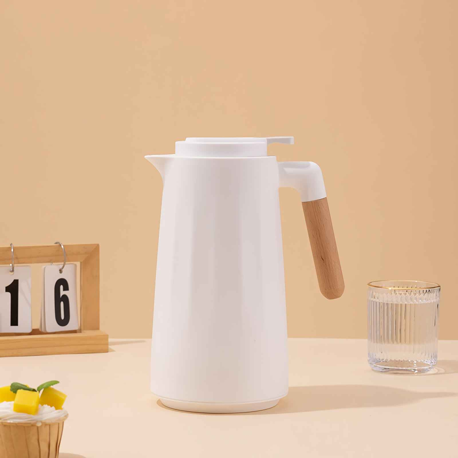 Eine weiße Thermoskanne mit Holzgriff neben einem Glas Wasser und einem Cupcake.