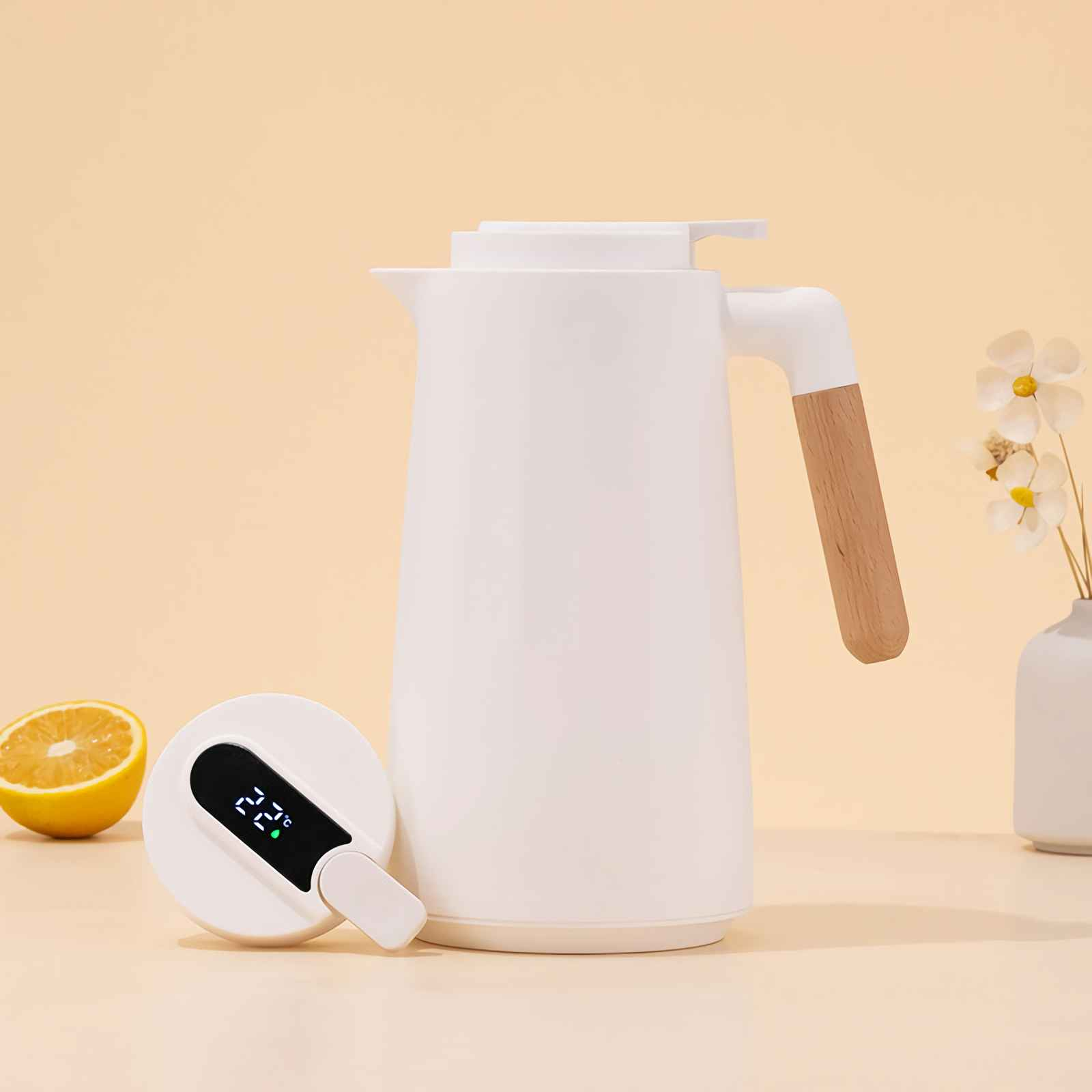 Weiße Thermoskanne mit Holzgriff, daneben eine aufgeschnittene Orange und eine Vase mit Blumen.