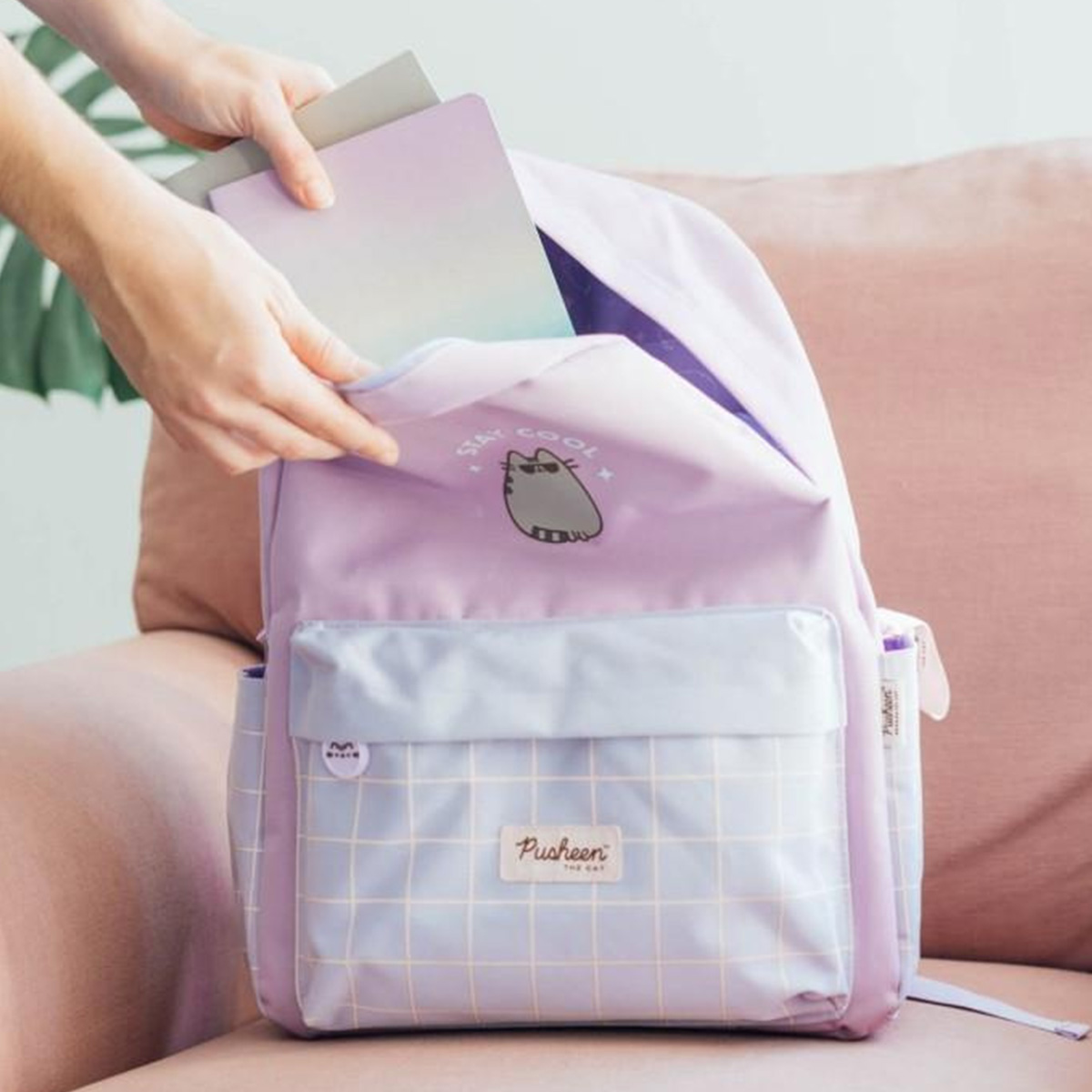 Mani mettono quaderni in uno zaino viola pastello con grafica di gatto Pusheen.