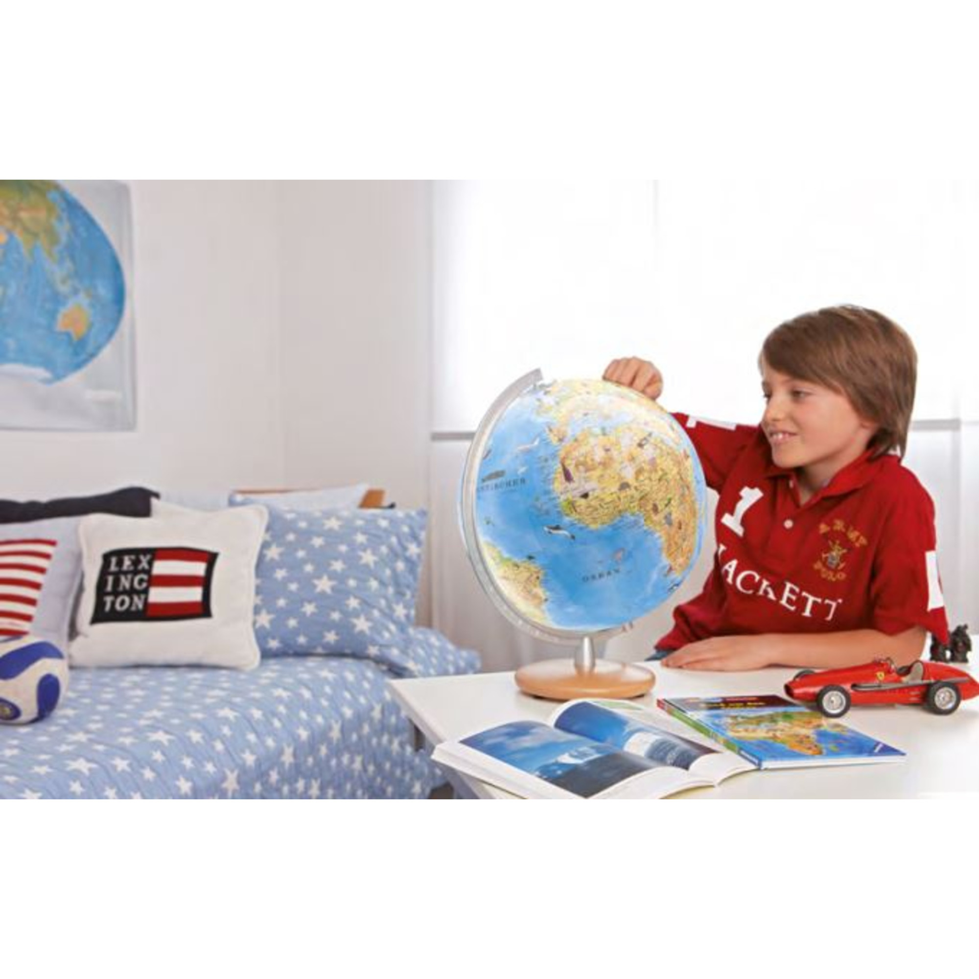 Junge mit Globus, Büchern und Spielzeugauto am Schreibtisch.