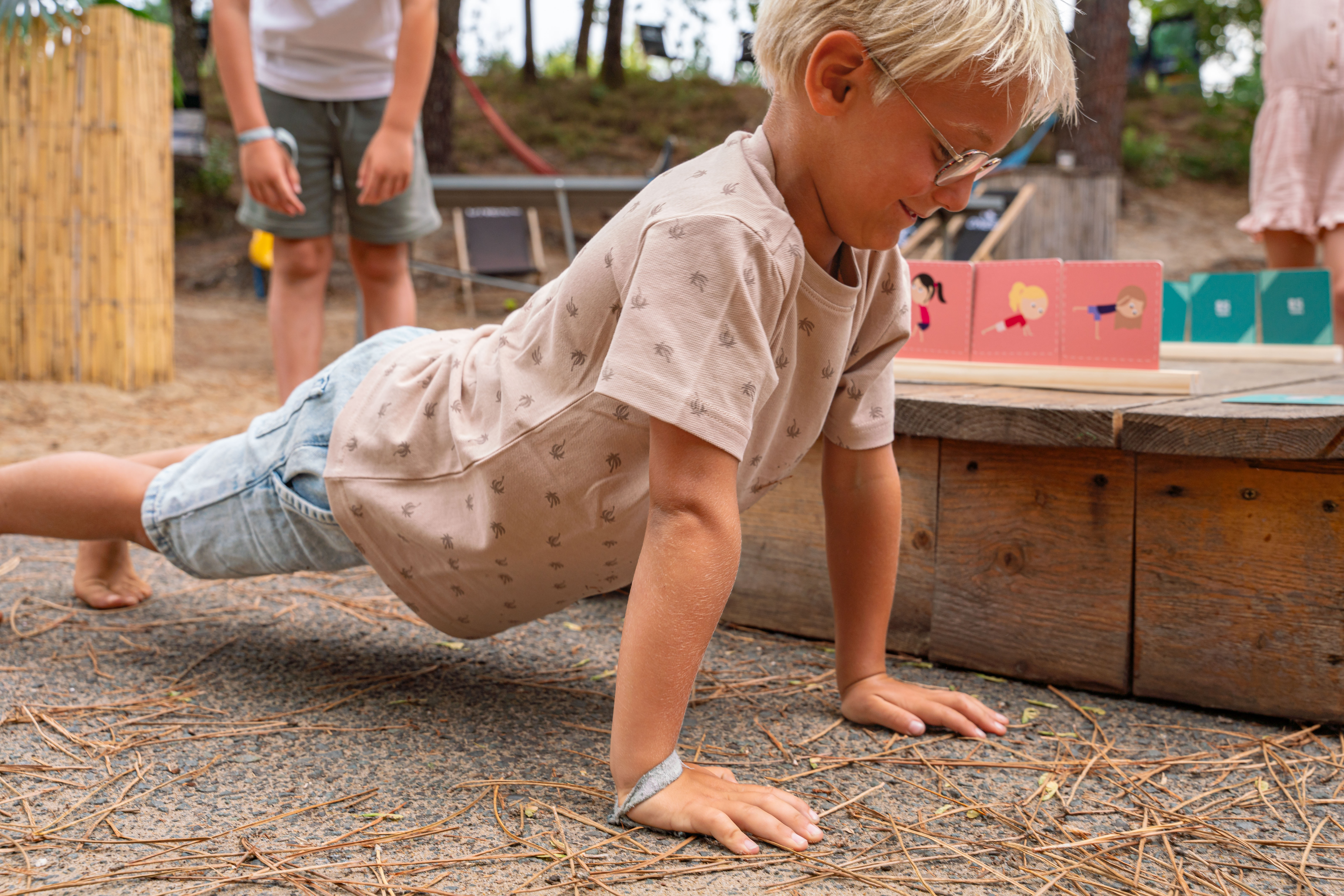 Een jongen in een korte broek en t-shirt doet een push-up op de grond.
