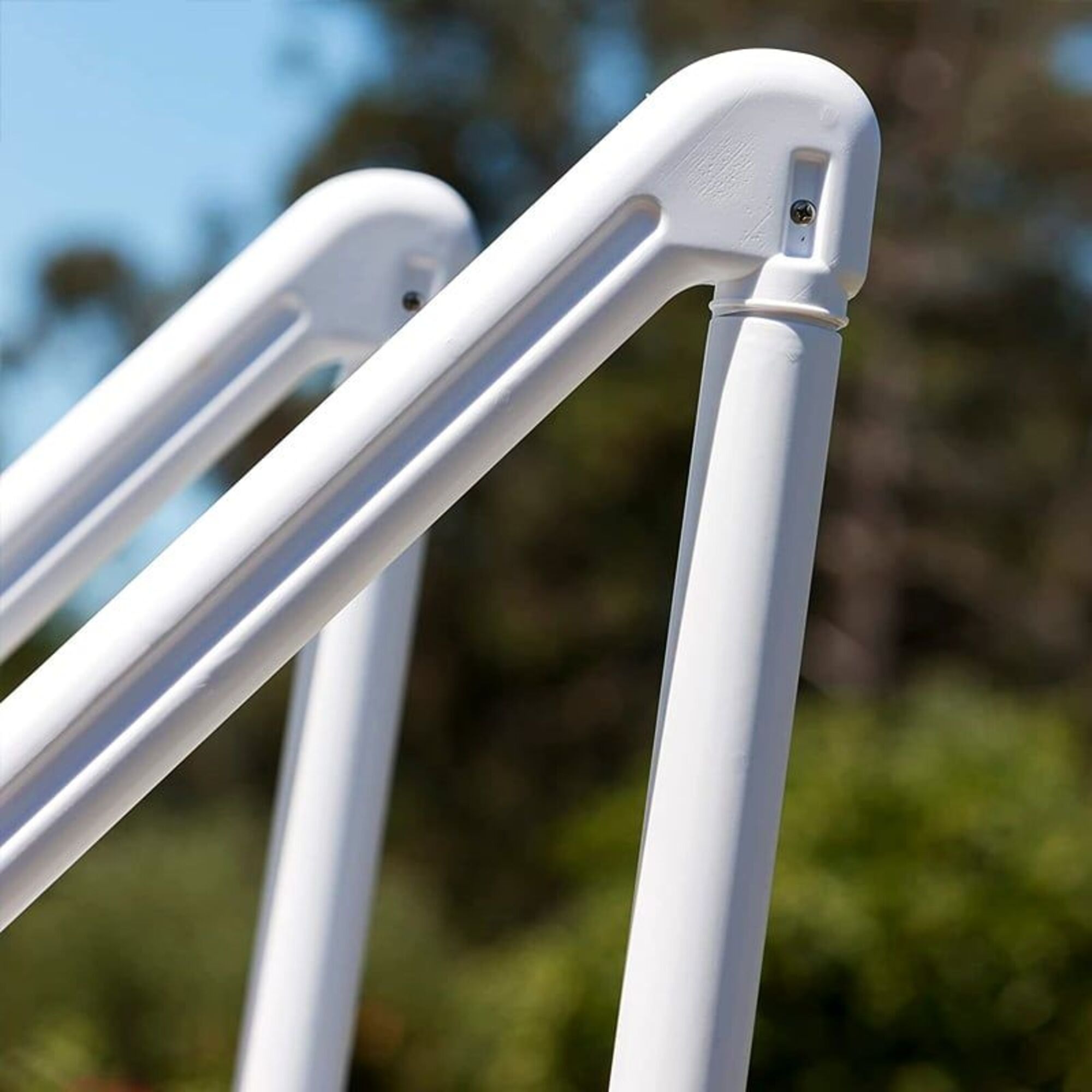 Corrimano bianco in plastica per piscina su sfondo verde e blu sfocato.