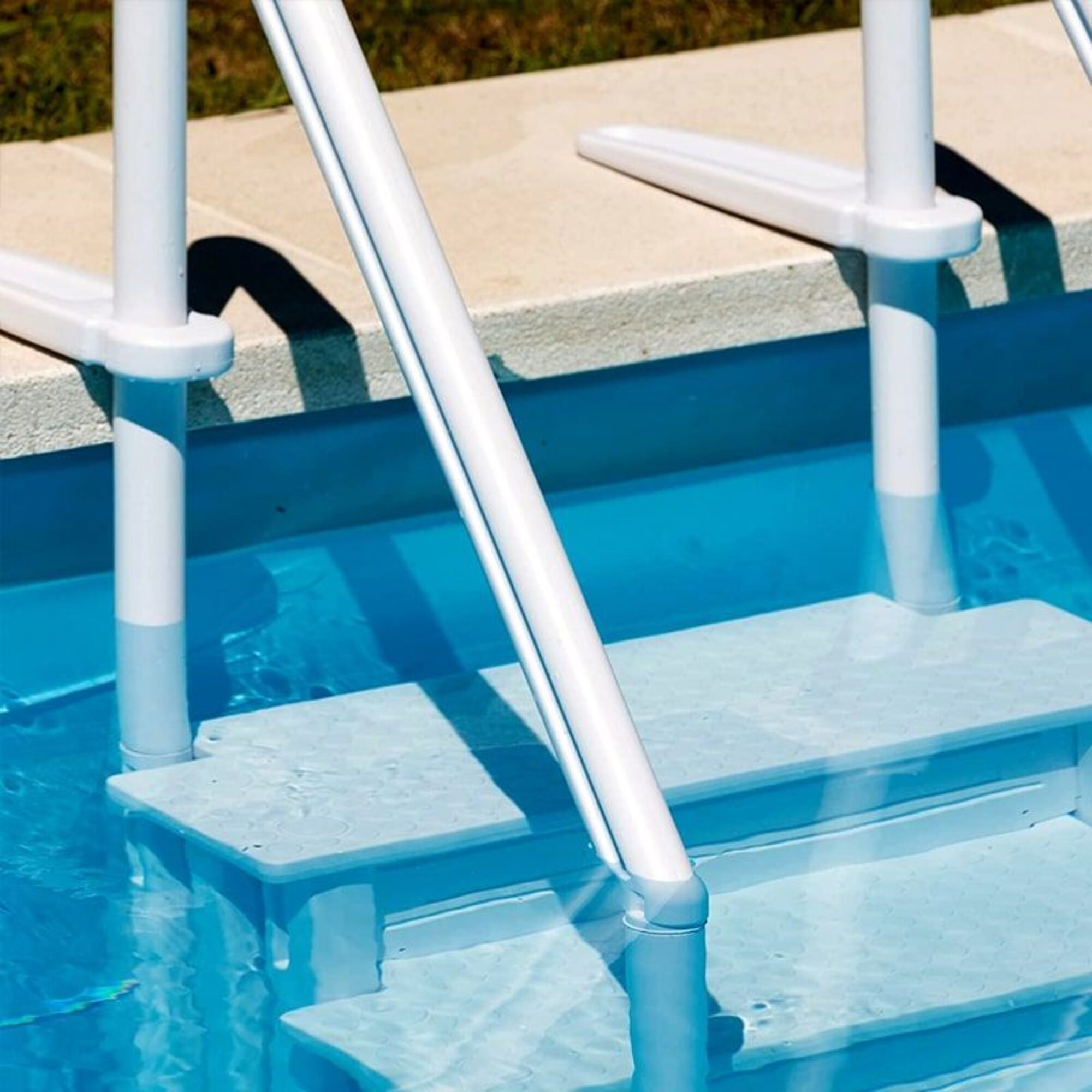 Scalini e corrimano bianchi per piscina in acqua blu limpida con bordo in cemento.