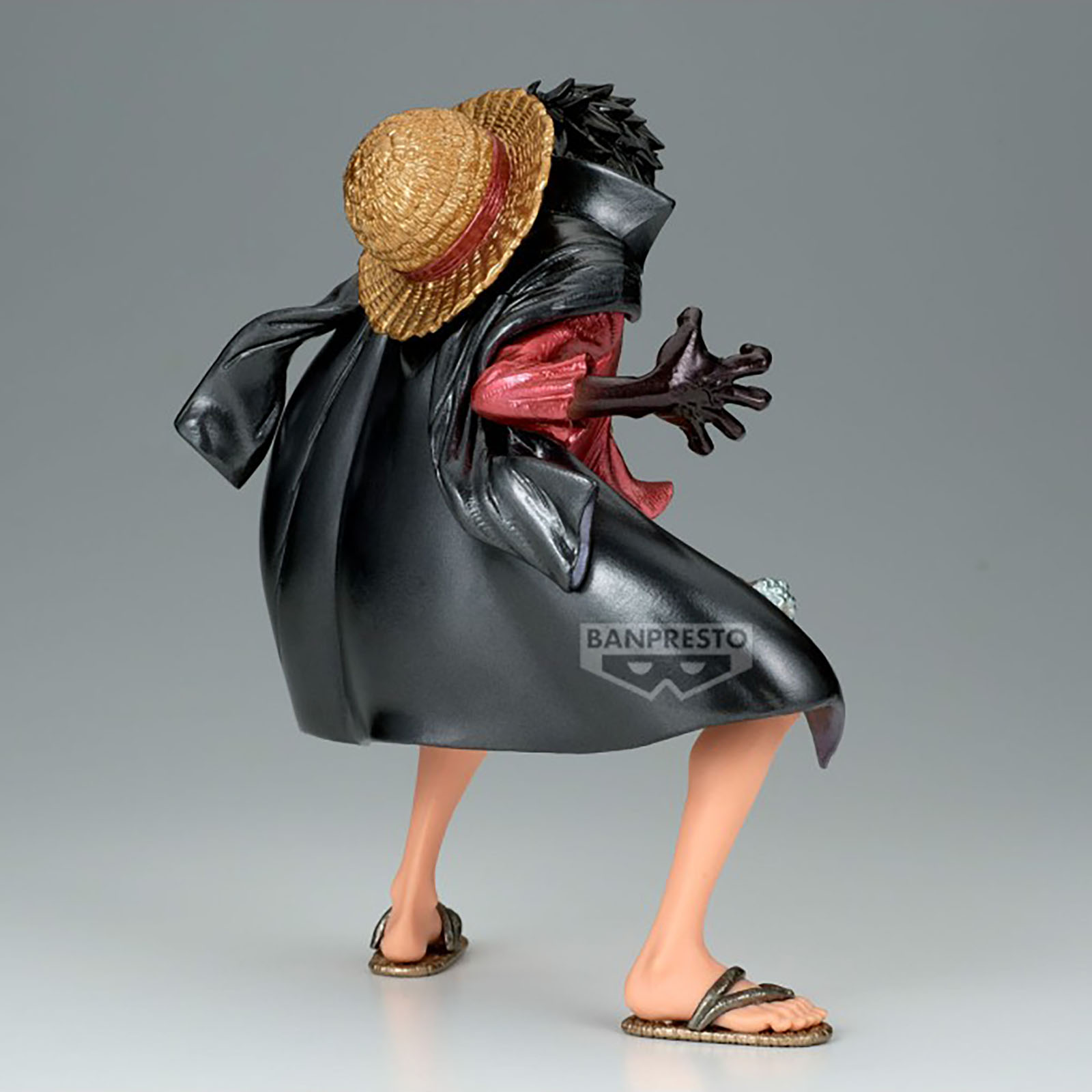 Eine Figur mit schwarzem Mantel, rotem Hemd und Strohhut, die Sandalen trägt.