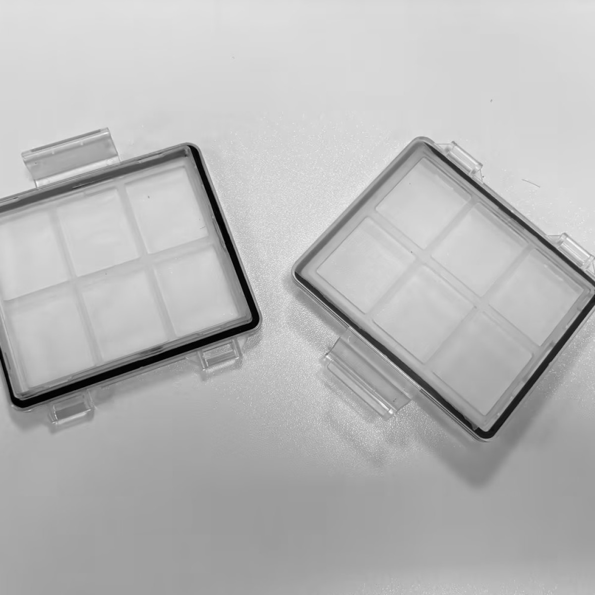 Dwa przezroczyste plastikowe filtry z białym siatkowym wkładem na białej powierzchni.