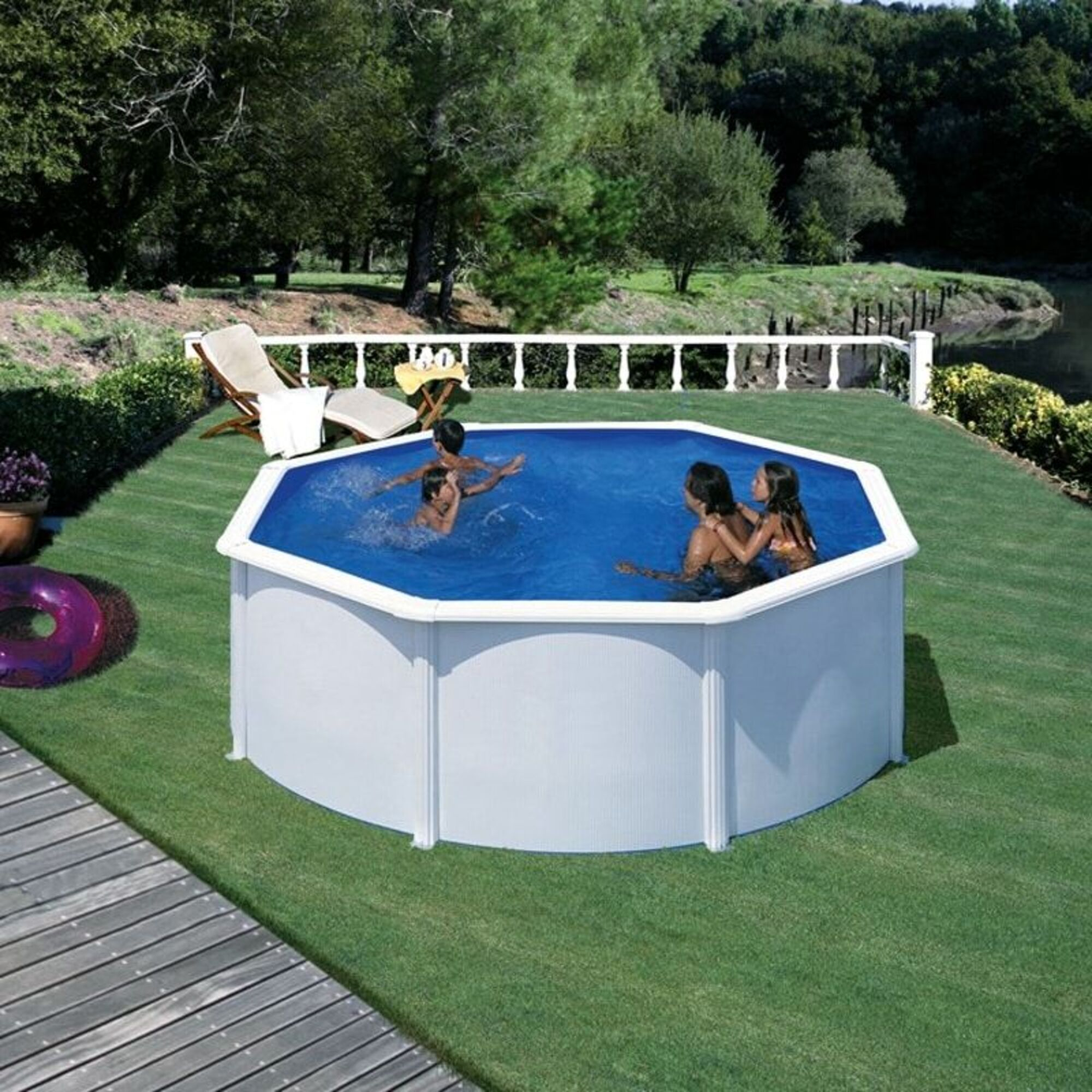 Una piscina octogonal con agua azul, cuatro personas chapoteando. Rodeada de césped verde.