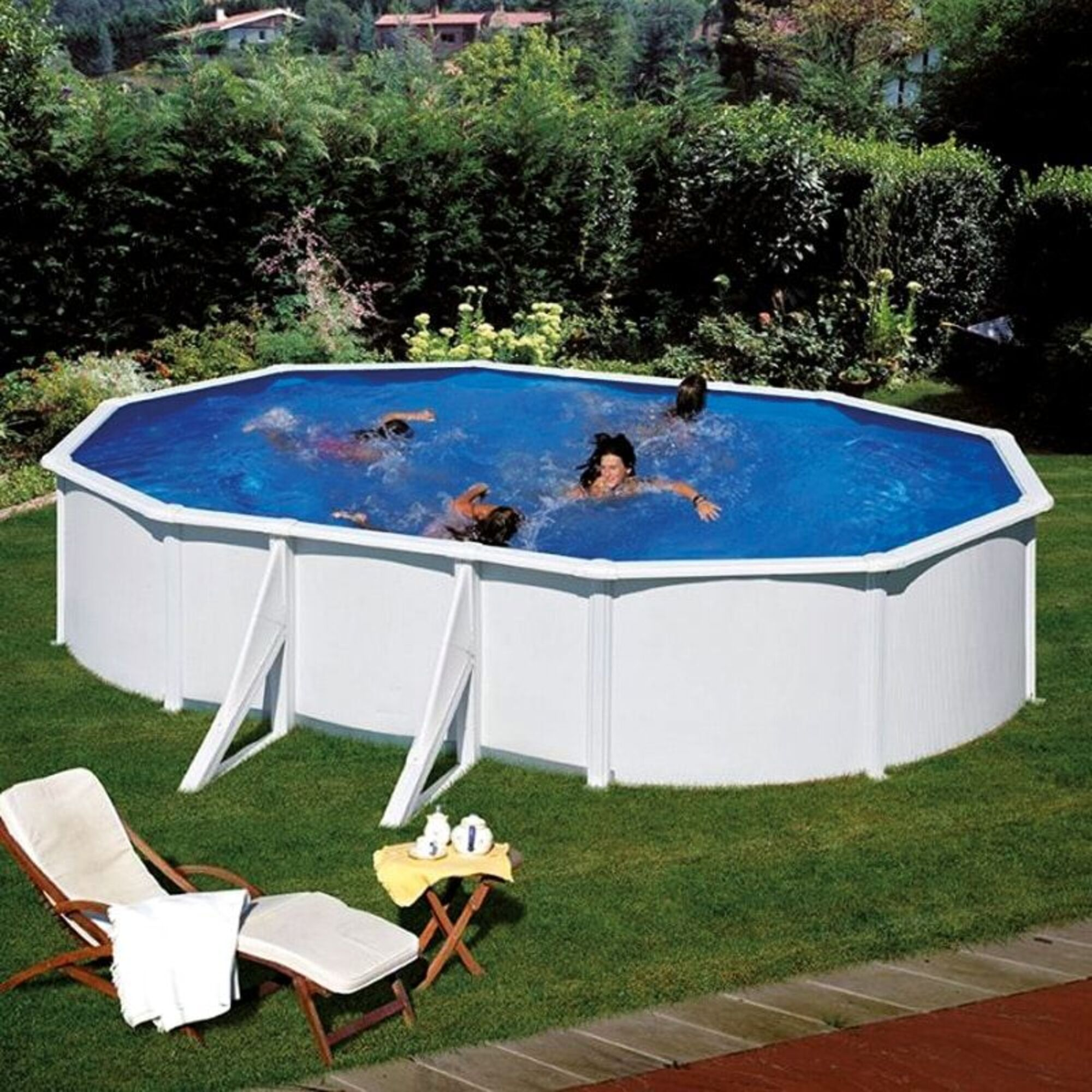 Personas nadan en una piscina ovalada rodeada de césped verde y árboles. Una tumbona está cerca.
