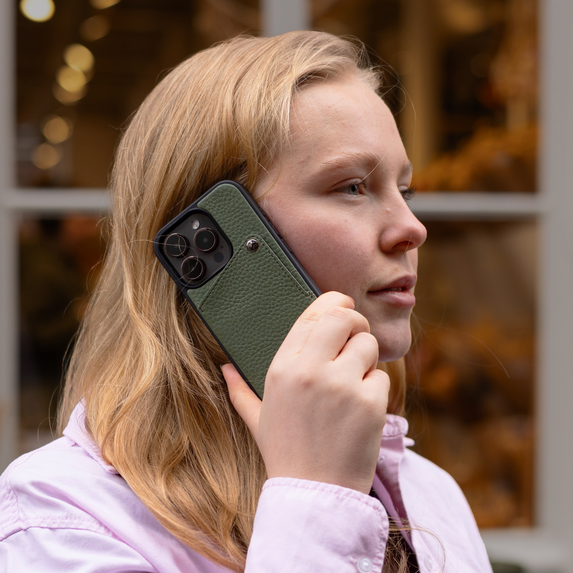 Une jeune femme aux cheveux blonds tient un téléphone vert à son oreille, porte une chemise rose.