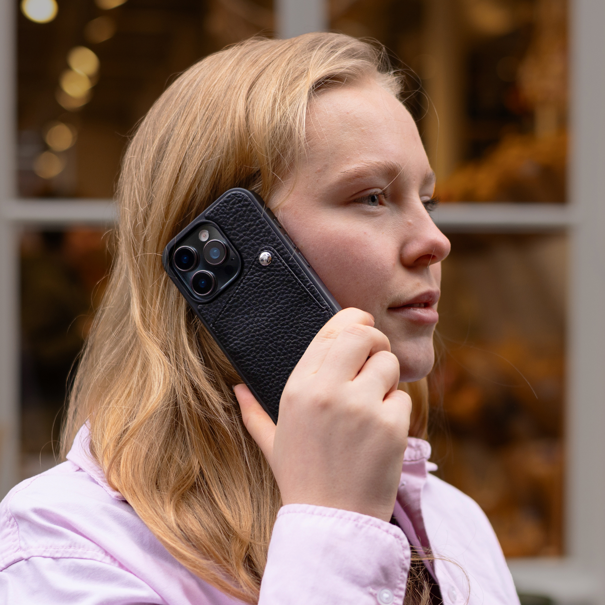 Une jeune femme blonde tient un téléphone noir à son oreille, portant une chemise rose.