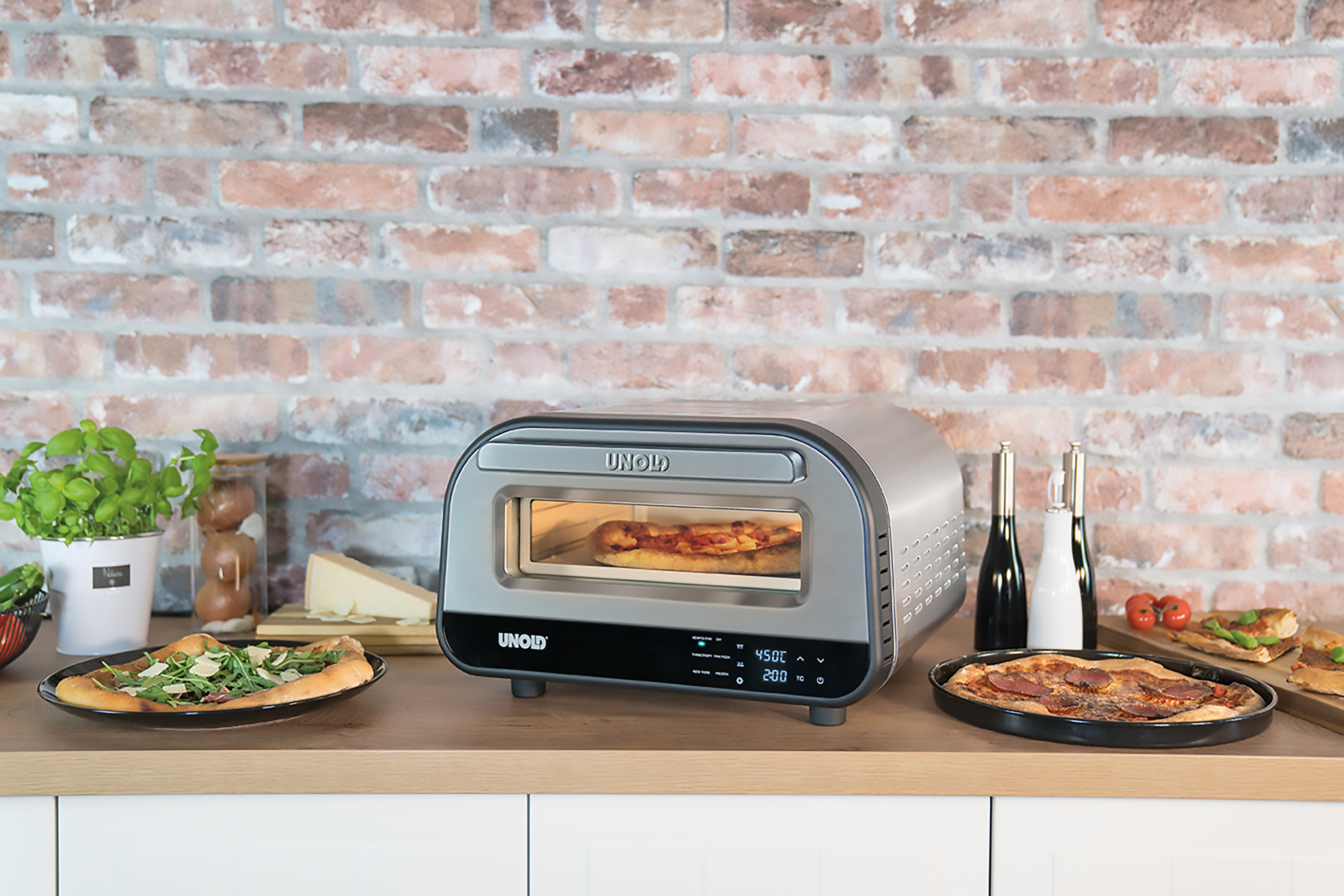 Un forno Unold cuoce una pizza. Sul bancone ci sono due pizze, formaggio, basilico e bottiglie.