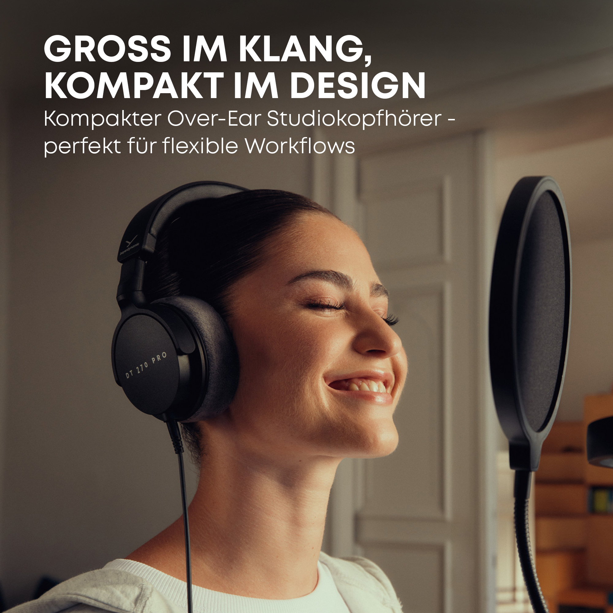 Eine Frau trägt schwarze Over-Ear-Kopfhörer, lächelt mit geschlossenen Augen, nahe einem Mikrofon.