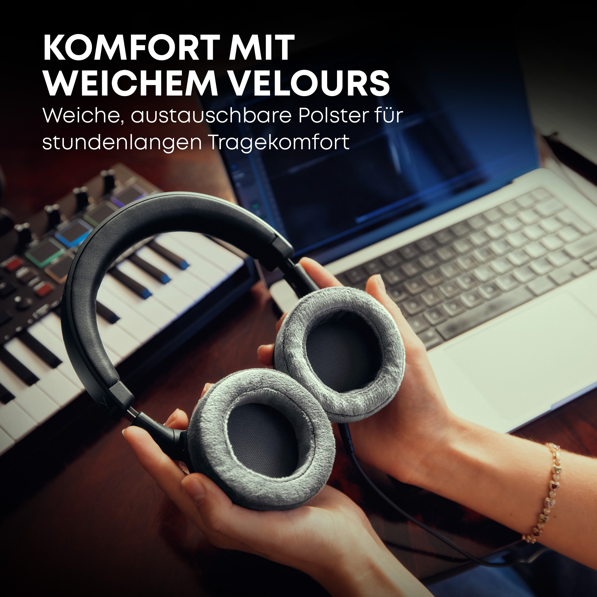 Hände halten graue Velour-Kopfhörer neben einem Laptop und einer Tastatur.