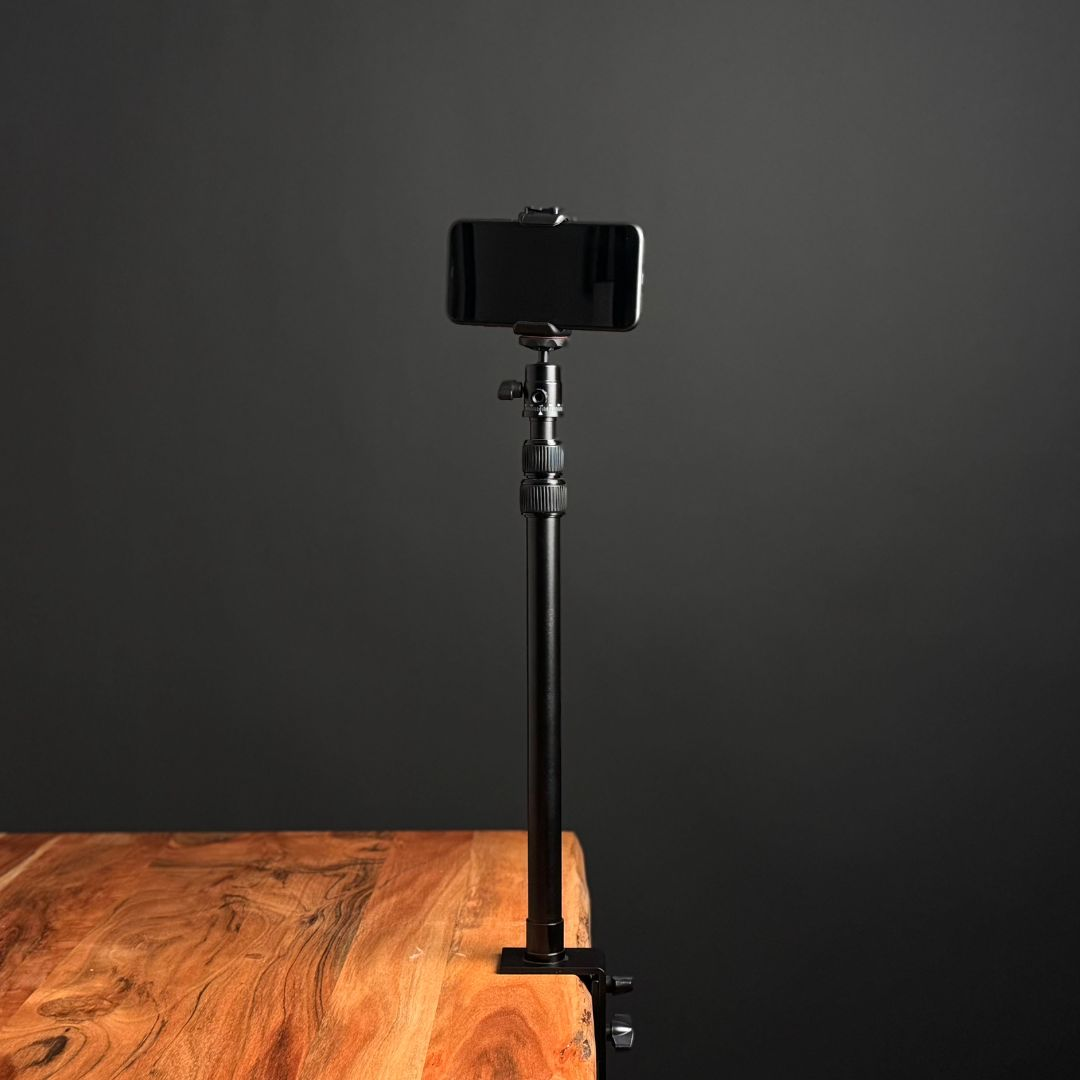A black smartphone holder on a stand attached to a wooden table, against a dark background.