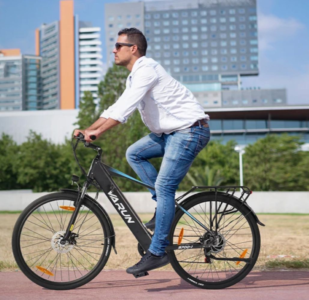Hombre con camisa blanca y jeans monta bicicleta eléctrica frente a edificios modernos.