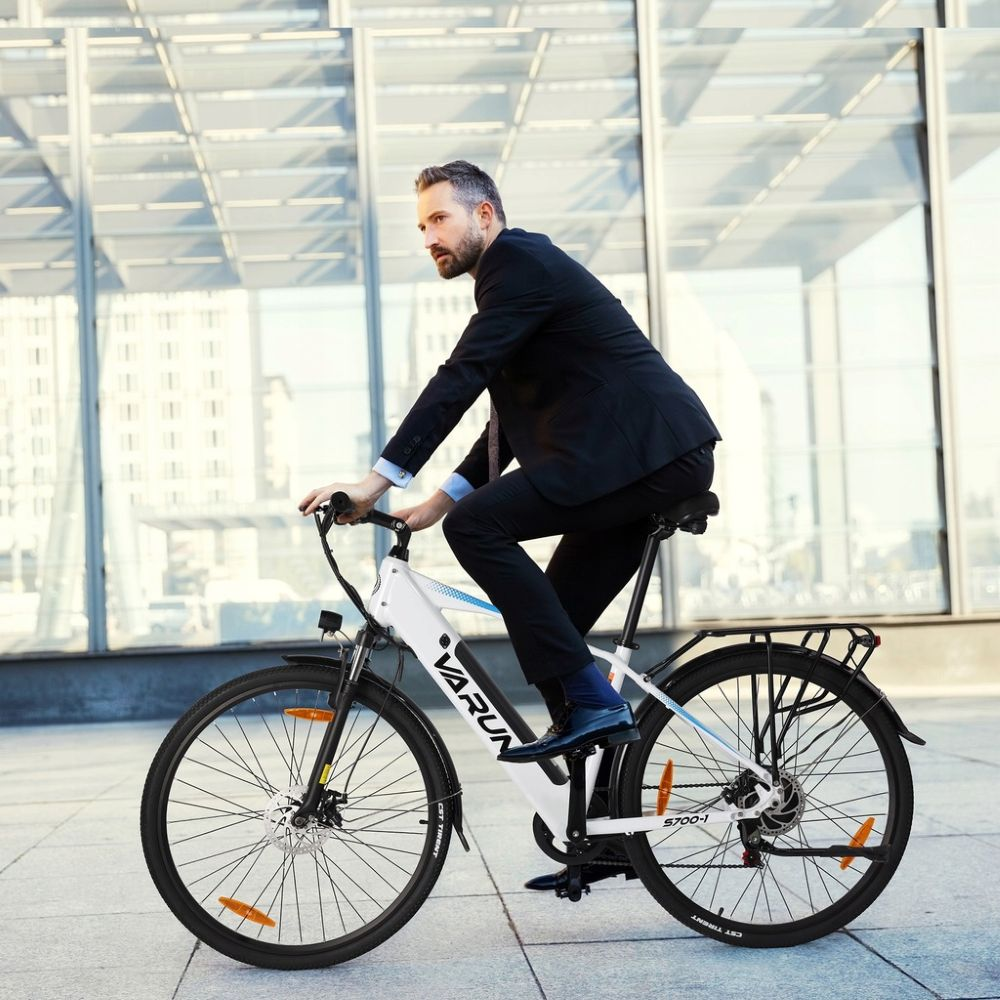 Hombre trajeado montando bici eléctrica blanca frente a edificio moderno cristal.