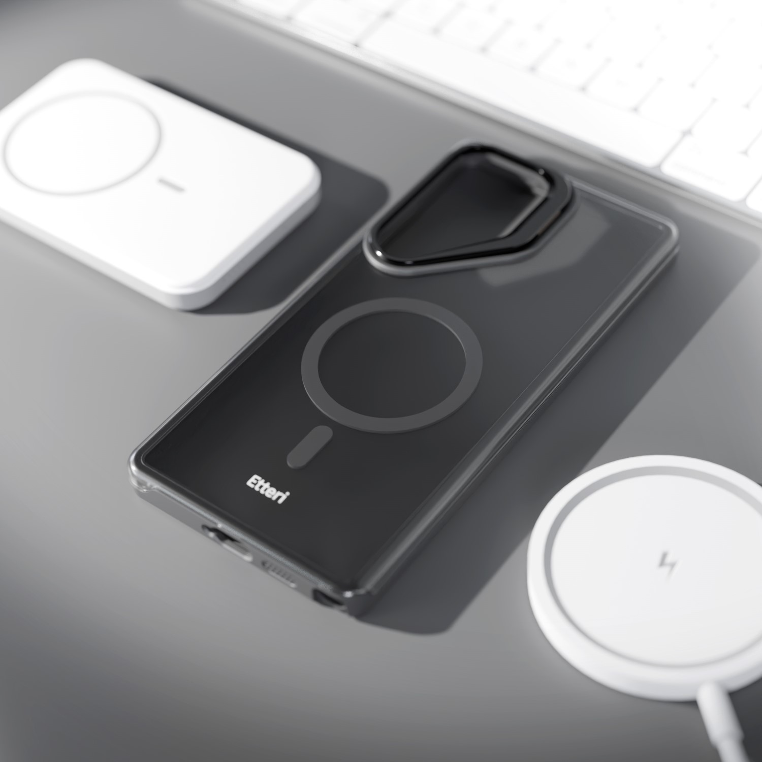 Una cover scura per telefono con anello magnetico giace accanto a due caricabatterie wireless bianchi.