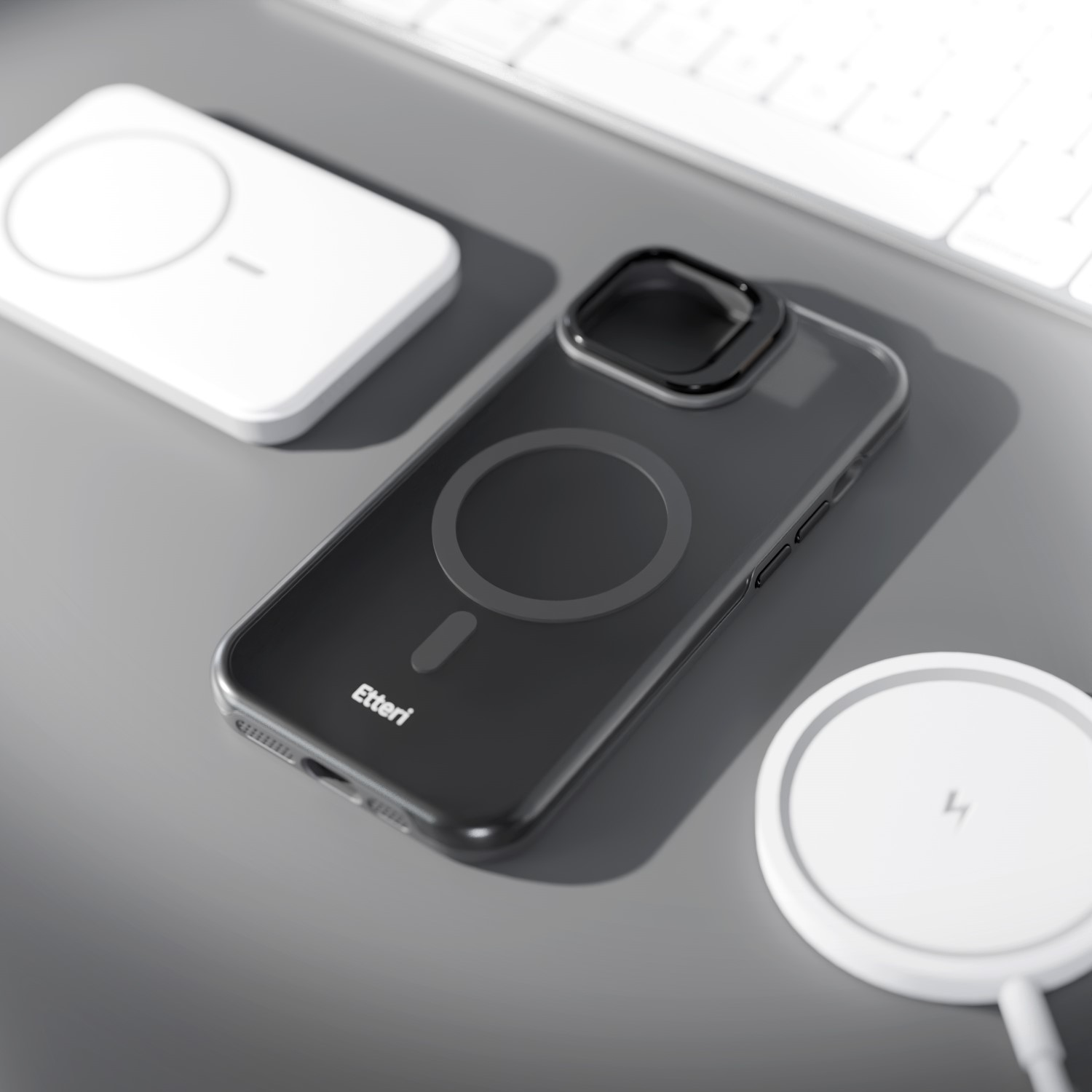 Czarne etui na telefon z magnetycznym pierścieniem leży na szarej powierzchni obok dwóch białych ładowarek bezprzewodowych.
