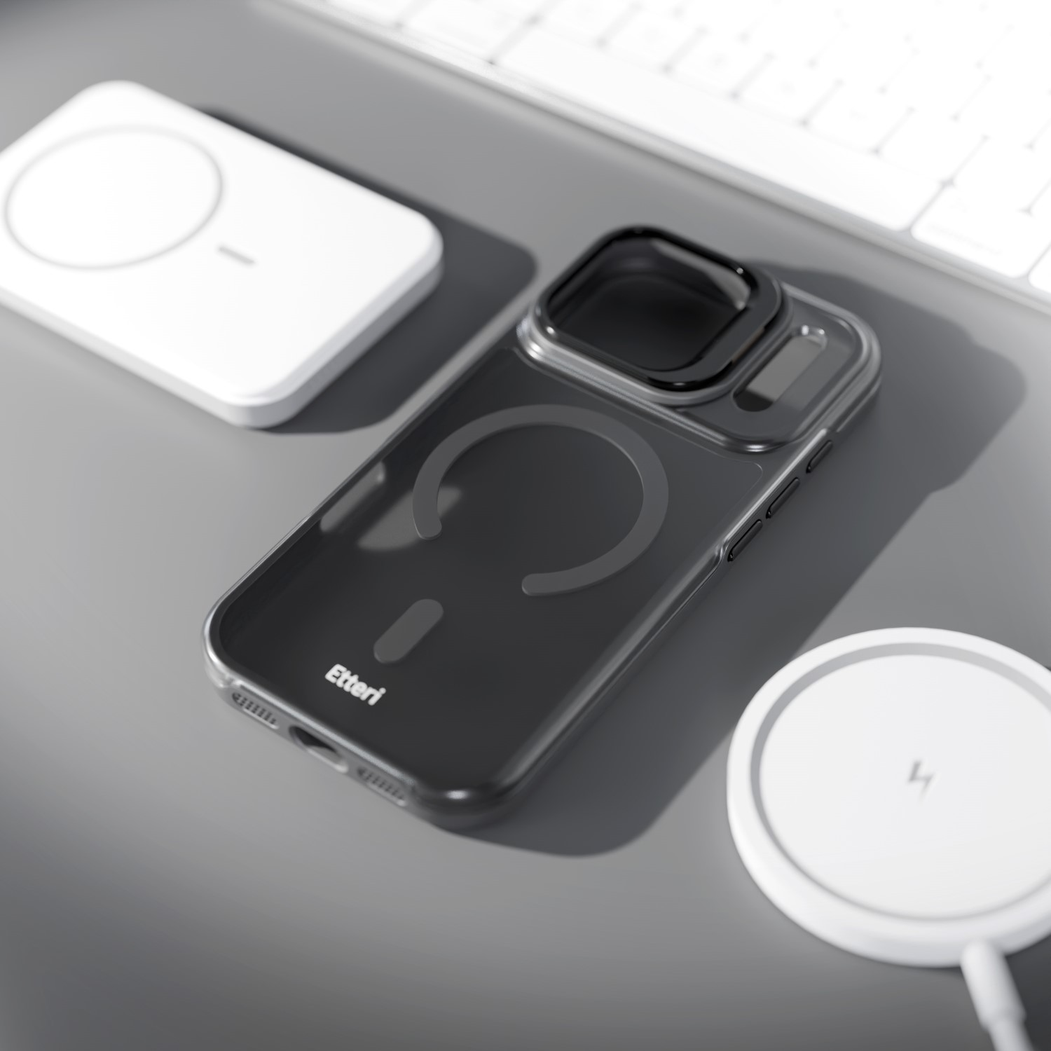 Una cover scura per telefono con anello magnetico su una superficie grigia vicino a tastiera e caricabatterie.