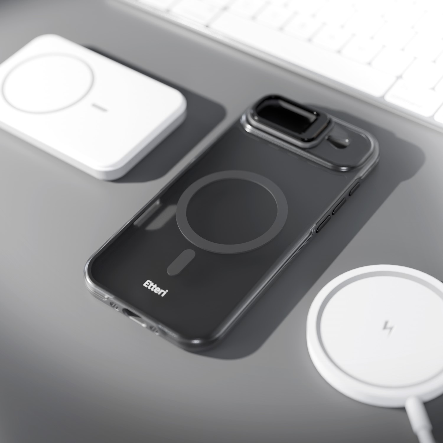 Ciemne etui na telefon z logo pierścienia magnetycznego leży na szarej powierzchni obok białych ładowarek.