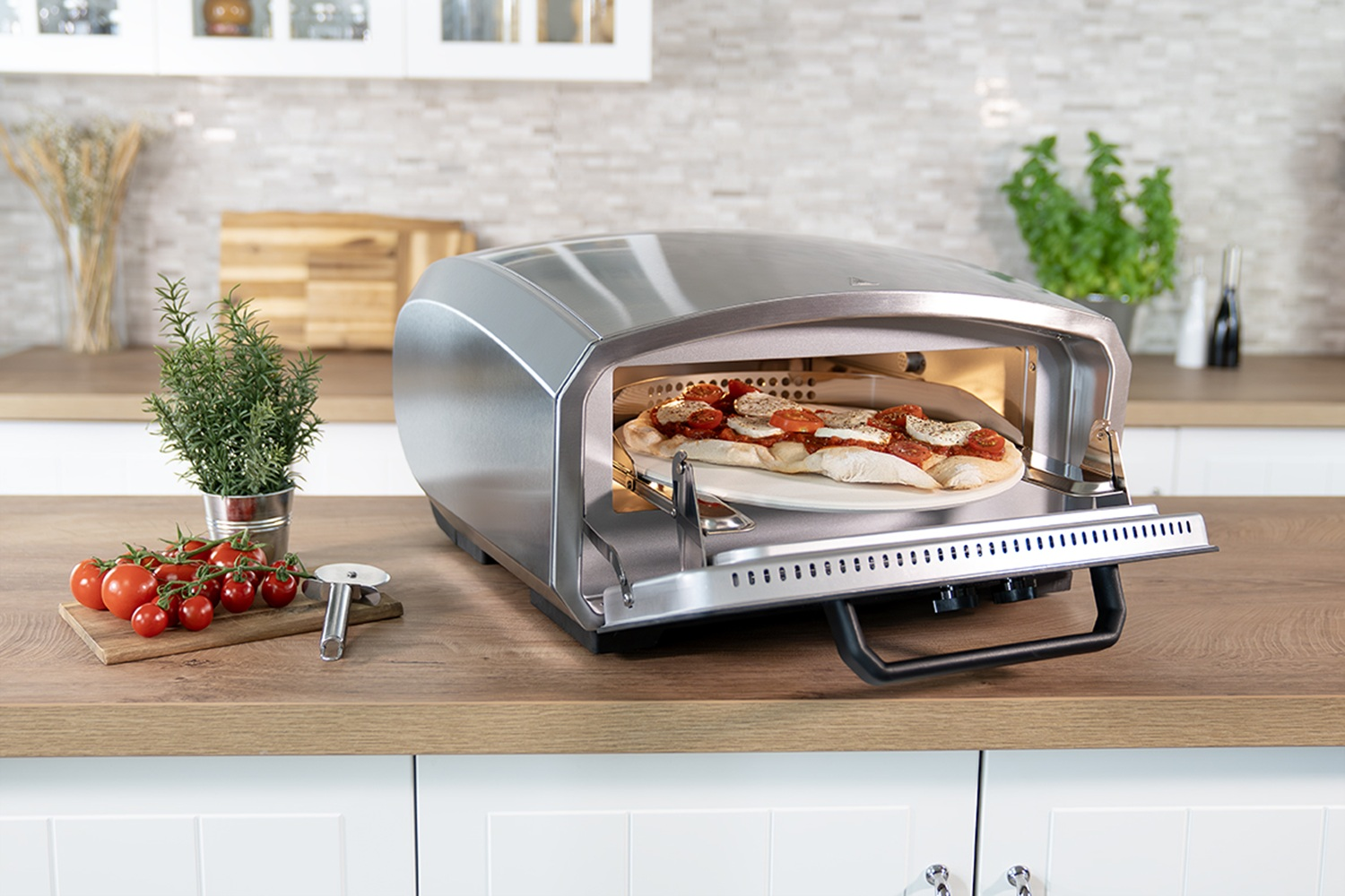 Eine Pizza mit Tomaten und Mozzarella gart in einem silbernen Pizzaofen auf einer Holztheke.
