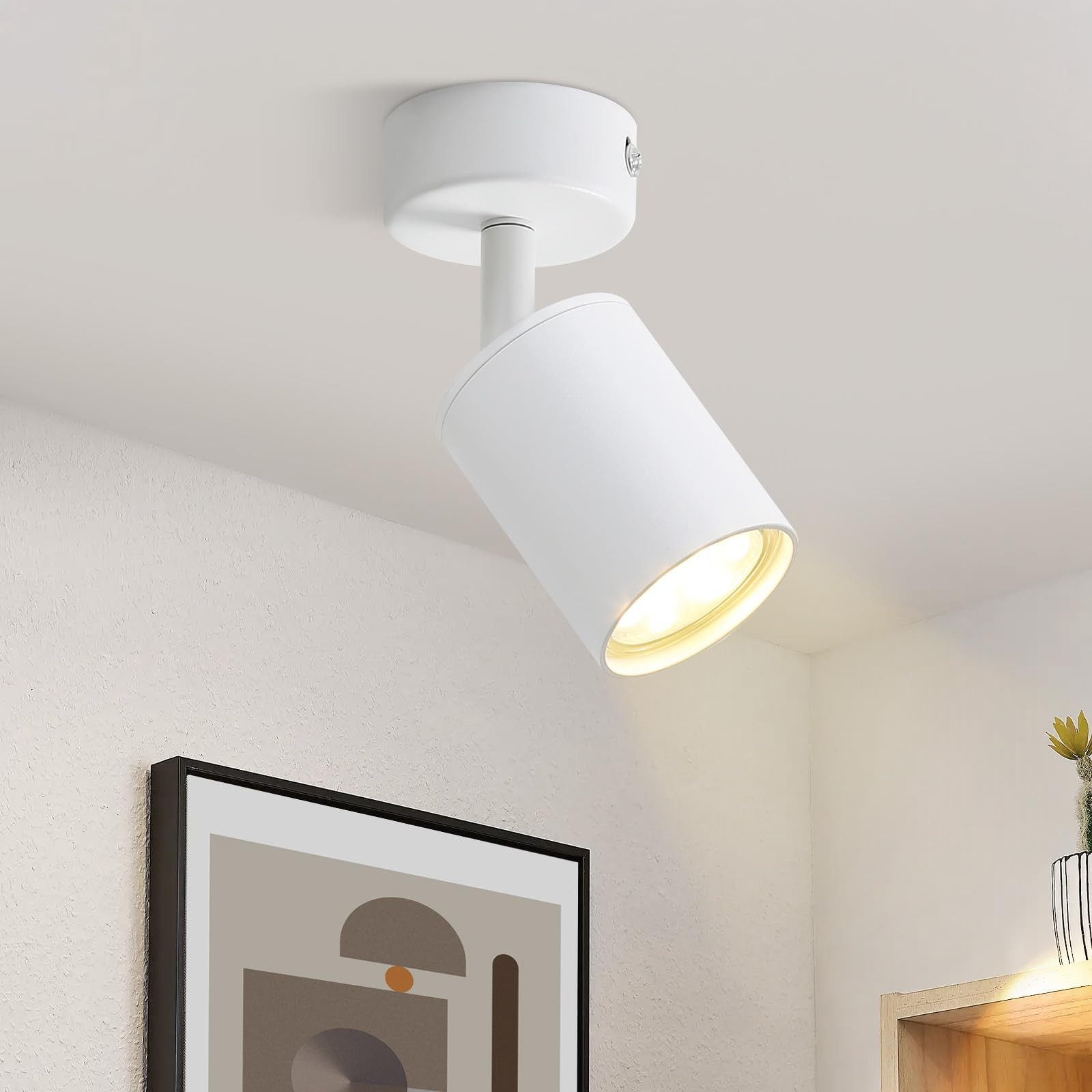 Un faretto da soffitto bianco illumina una parete testurizzata e un'opera d'arte astratta incorniciata.