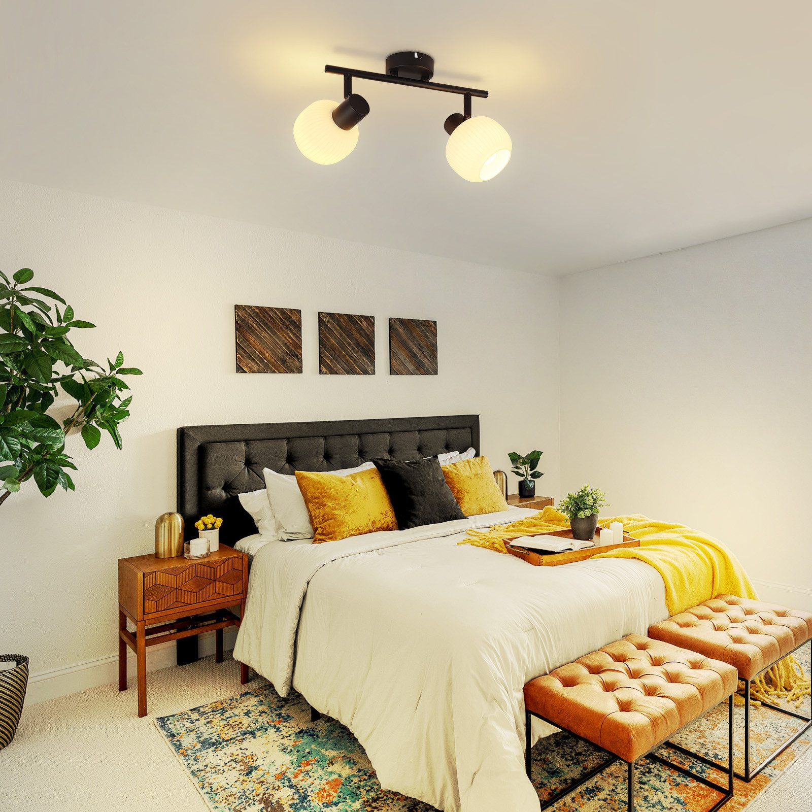 Una camera da letto con letto bianco, cuscini gialli e copriletto giallo. Due panche arancioni ai piedi del letto.