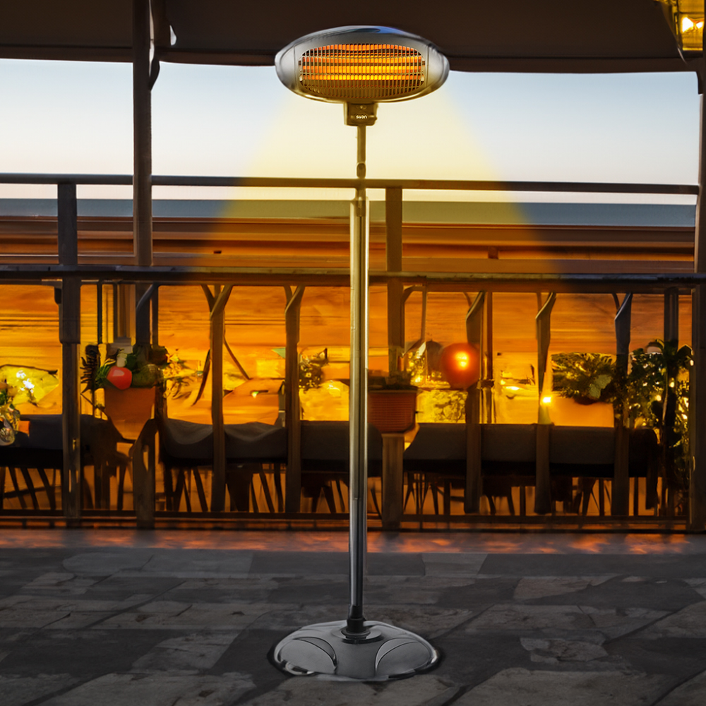 Un calentador alto para patio exterior con elemento naranja brillante se encuentra en un patio embaldosado al anochecer.