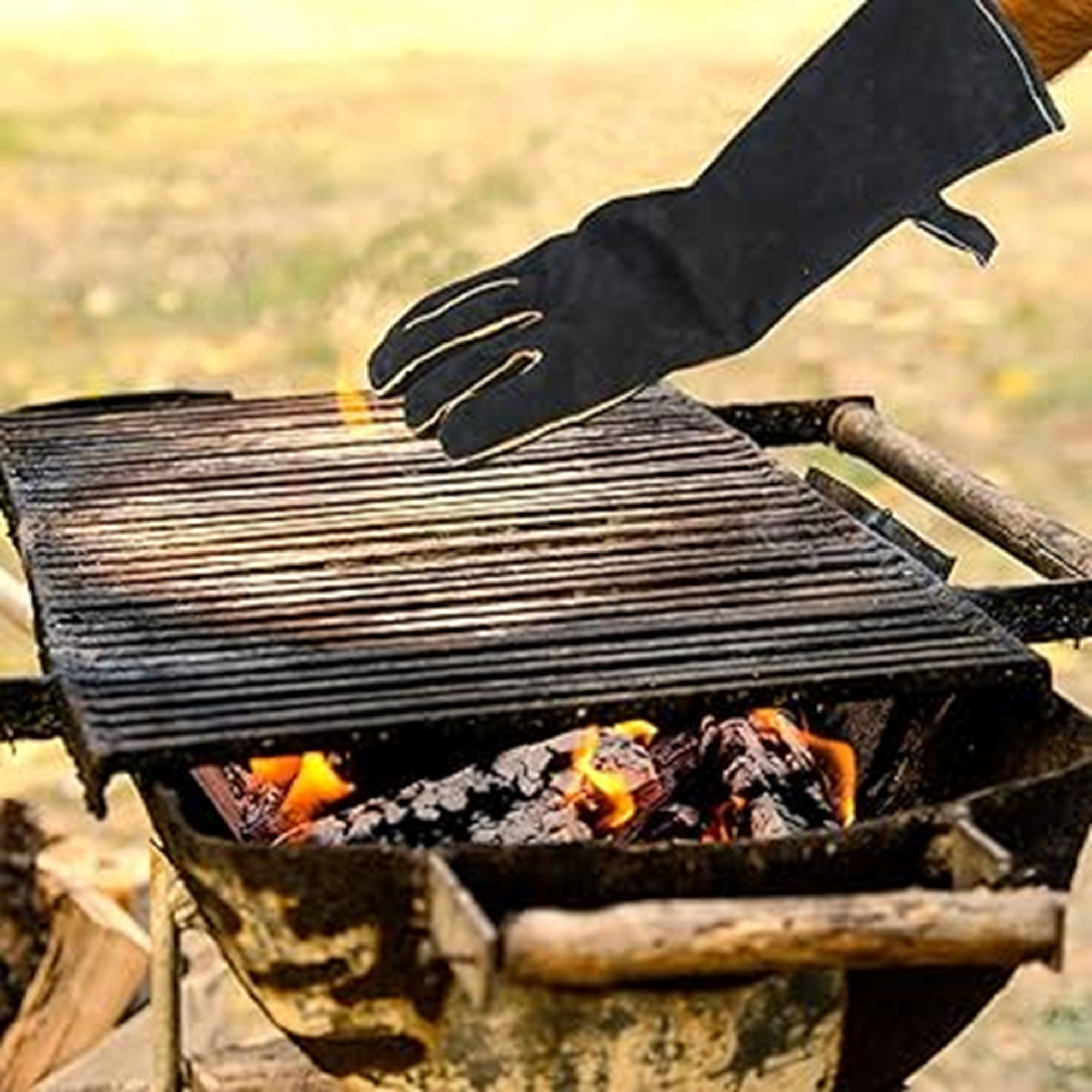 Mano con guante negro ajustando parrilla sobre brasas encendidas al aire libre.